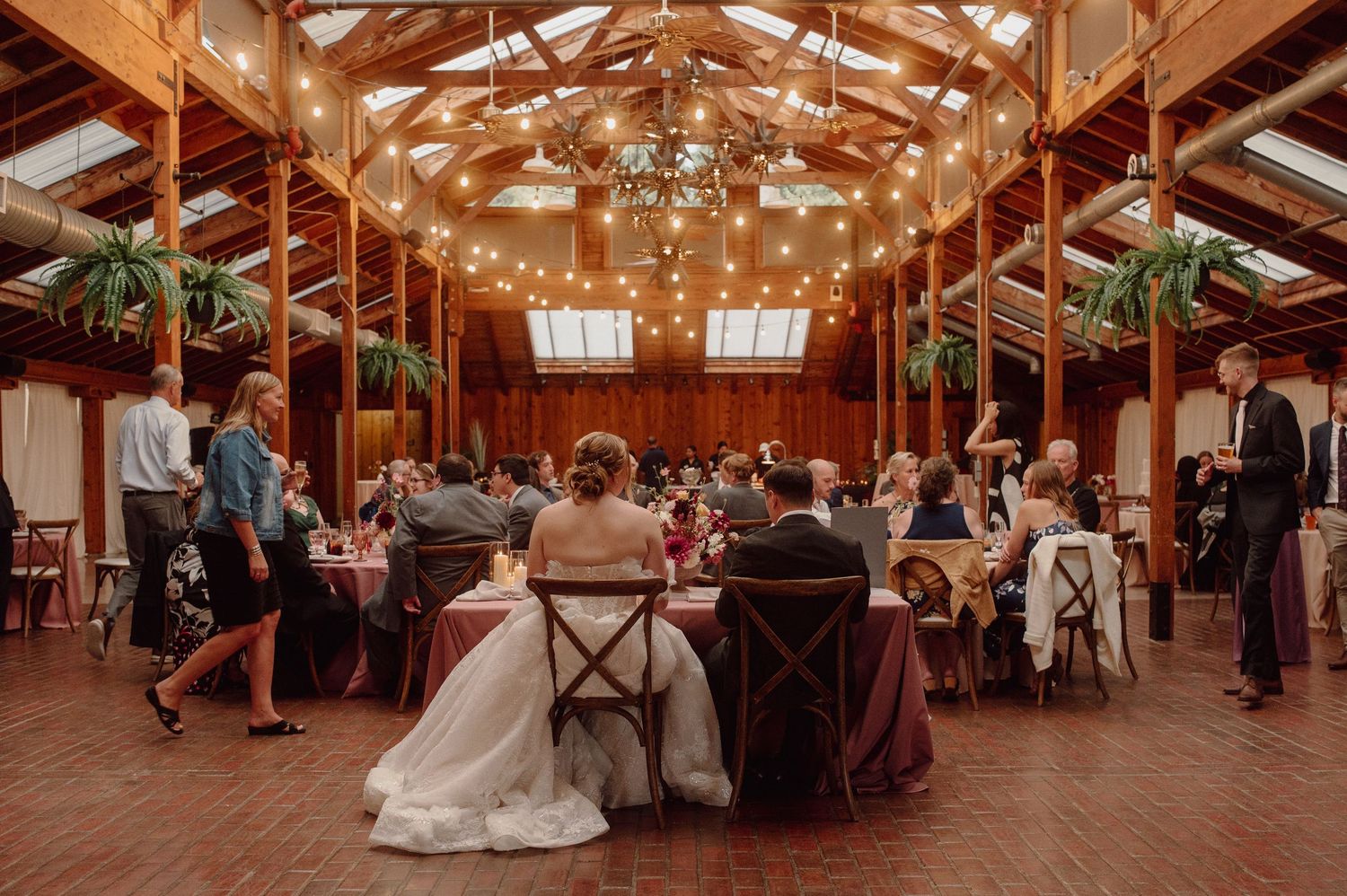 Rustic barn wedding reception venue with exposed wooden beams, string lights, and guests mingling on the dance floor.