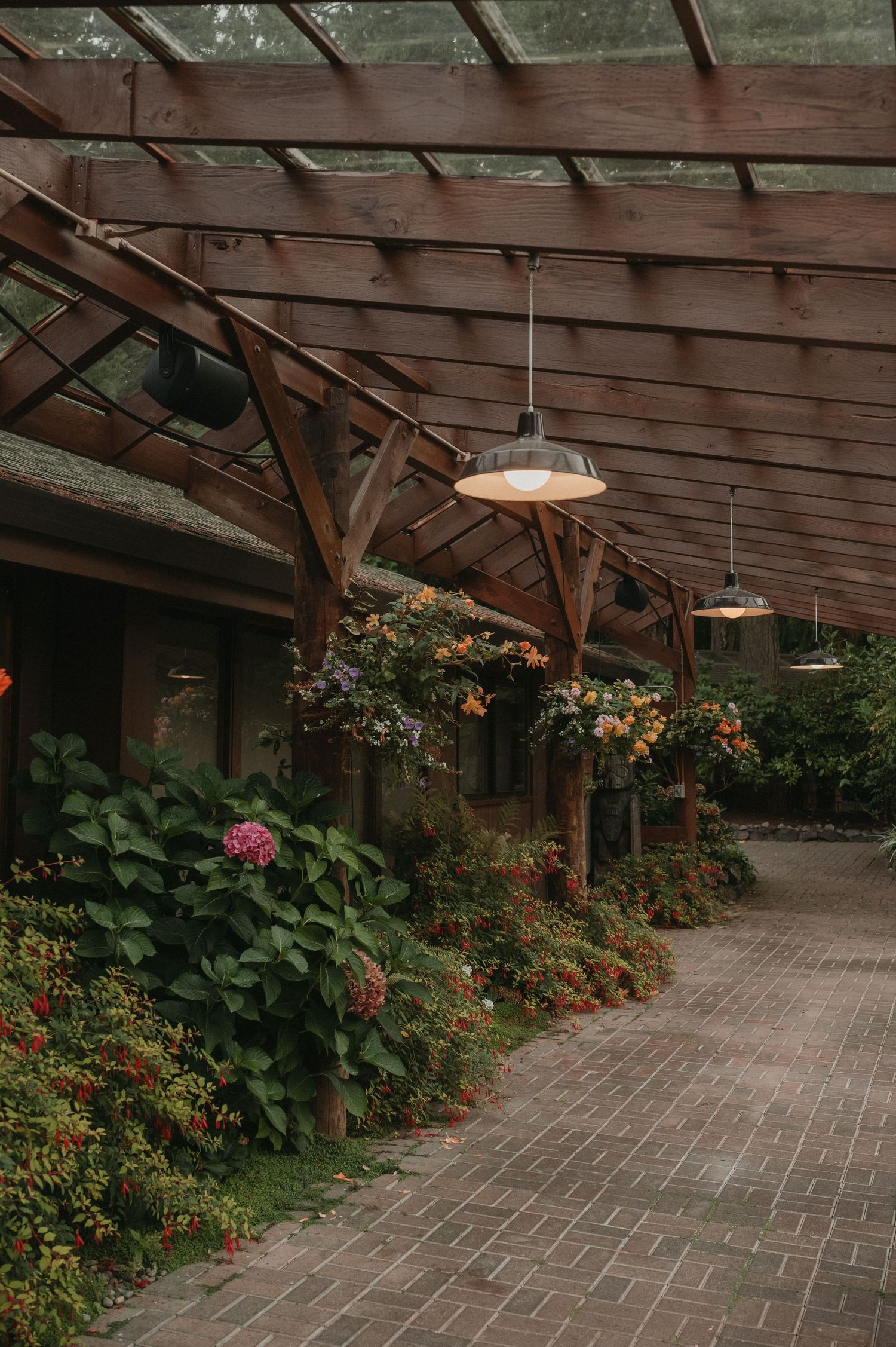 A rustic wooden covered walkway with hanging lights and colorful flowers growing along the sides.