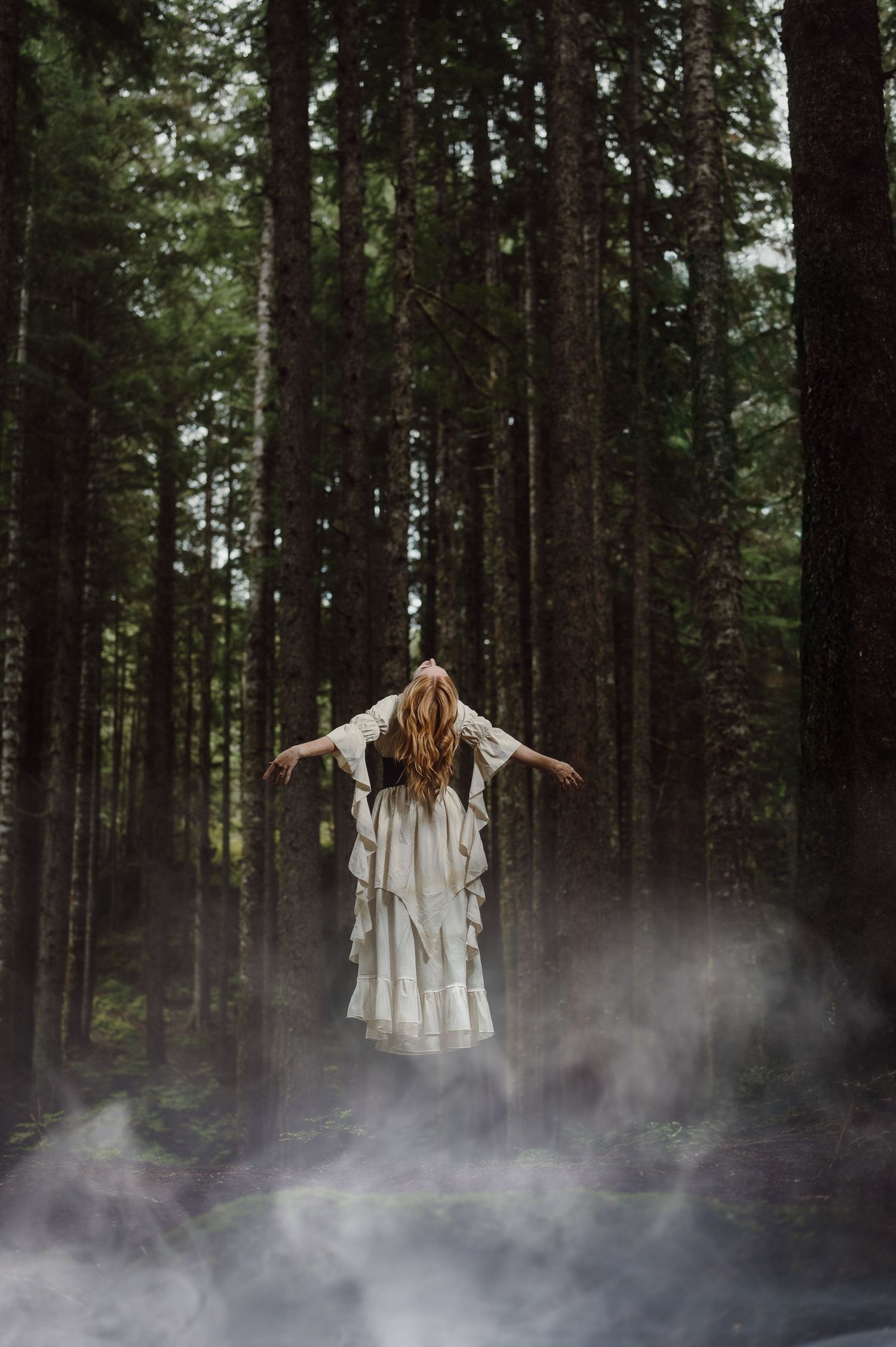 A person in white dress stands mysteriously in misty forest creating an ethereal atmosphere among tall pine trees.