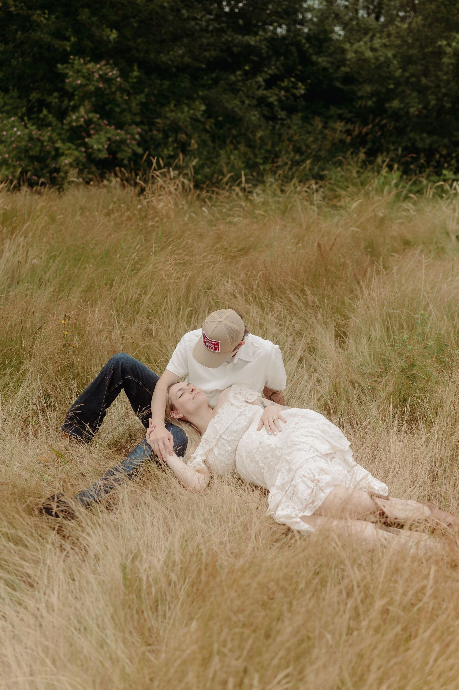 Couple sharing a romantic moment in a golden grass field, woman in white lace dress lying back as man leans in to kiss her.