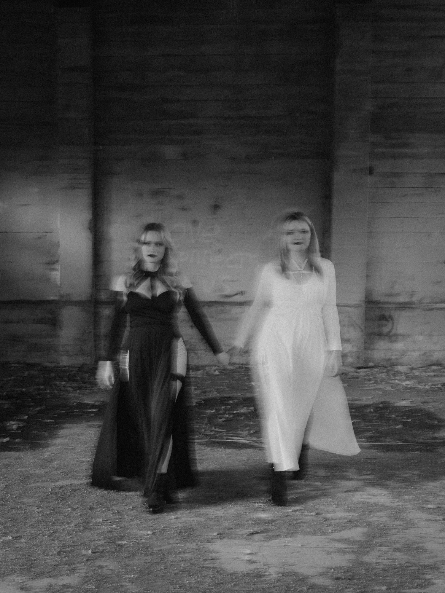 Multiple blurry black and white figures moving in a dark interior space create an eerie ghost-like atmosphere.