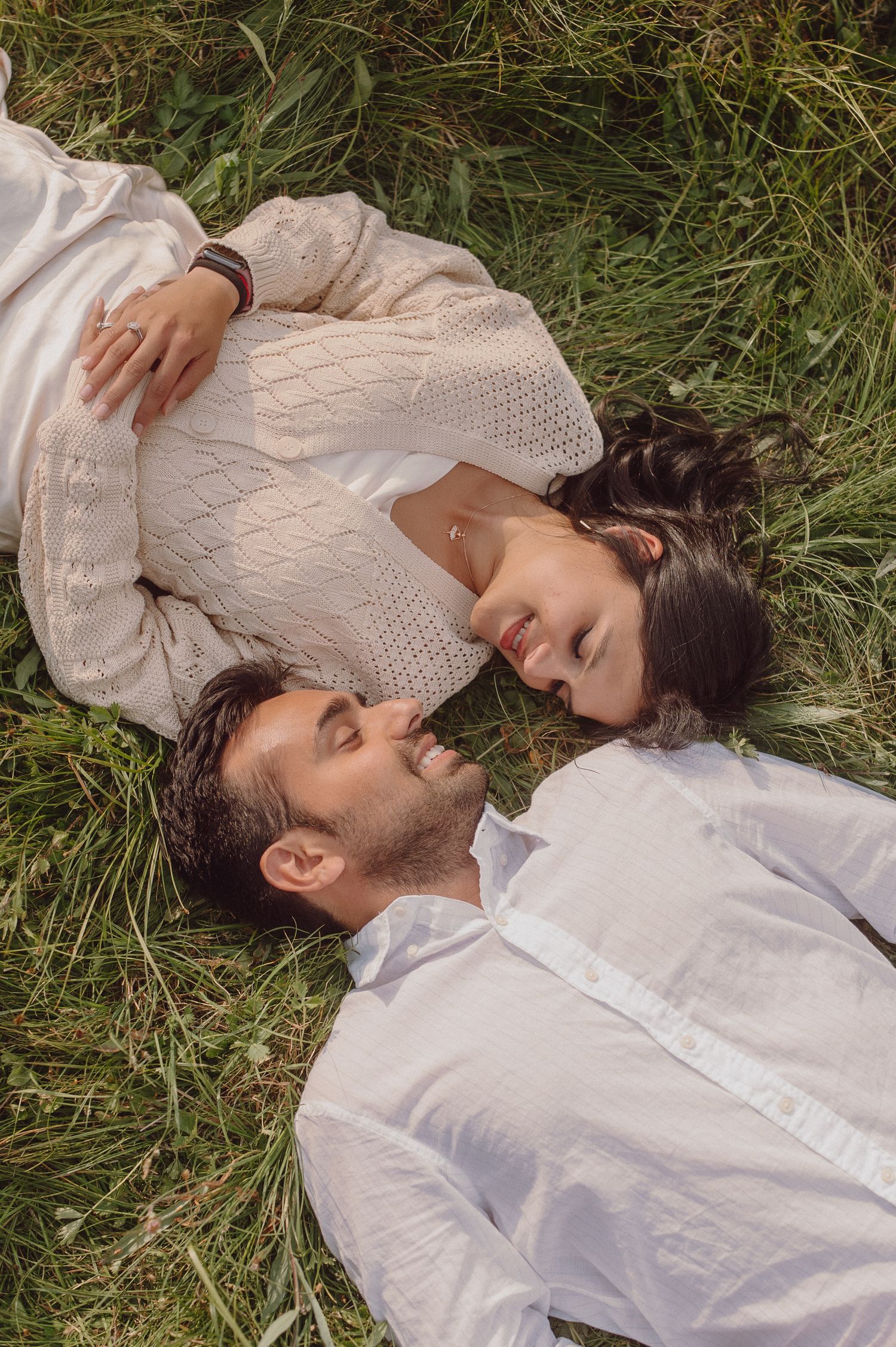 A couple lying in tall grass together during an intimate outdoor photoshoot.