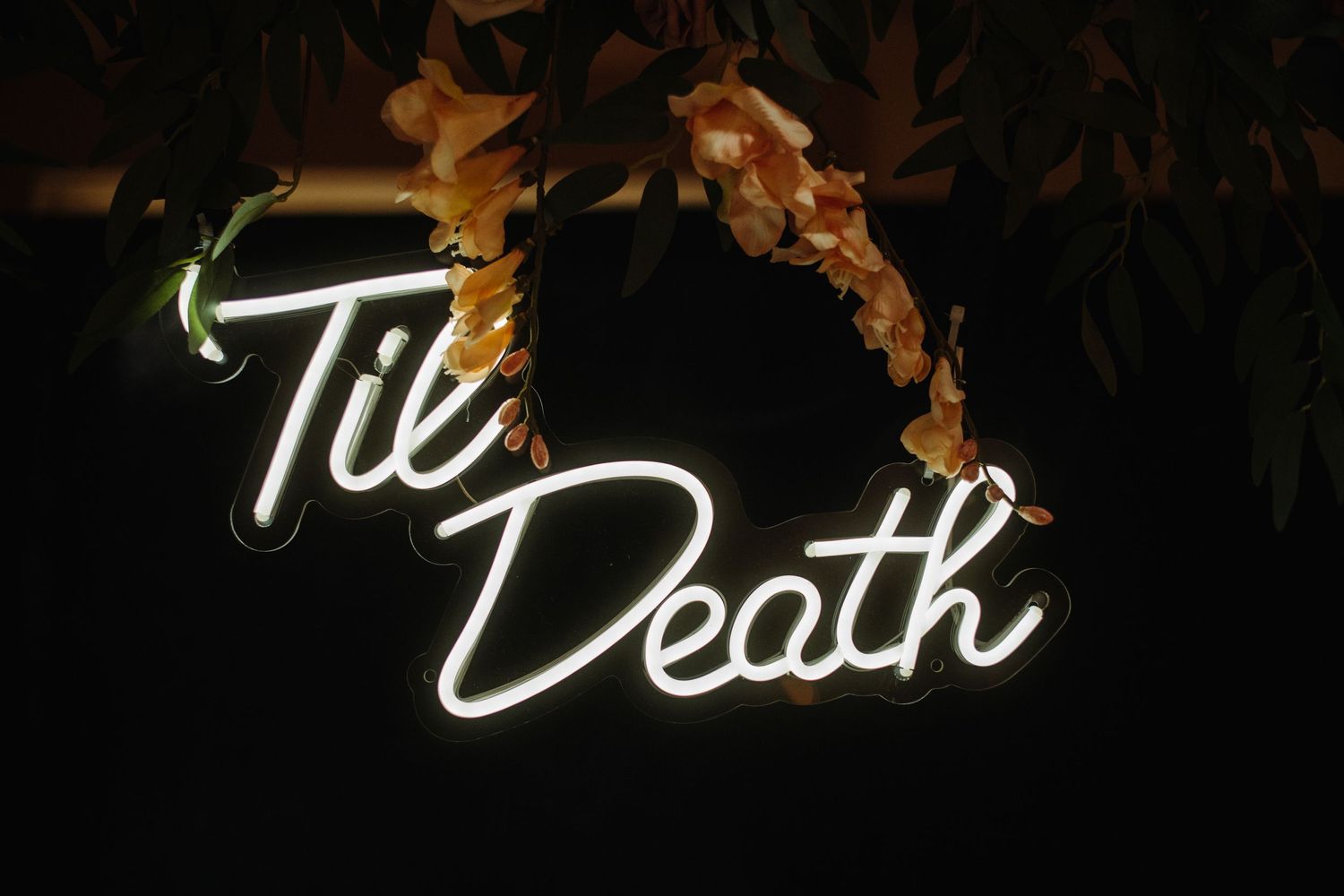 Neon sign reading 'Til Death' with flames effect against dark background.