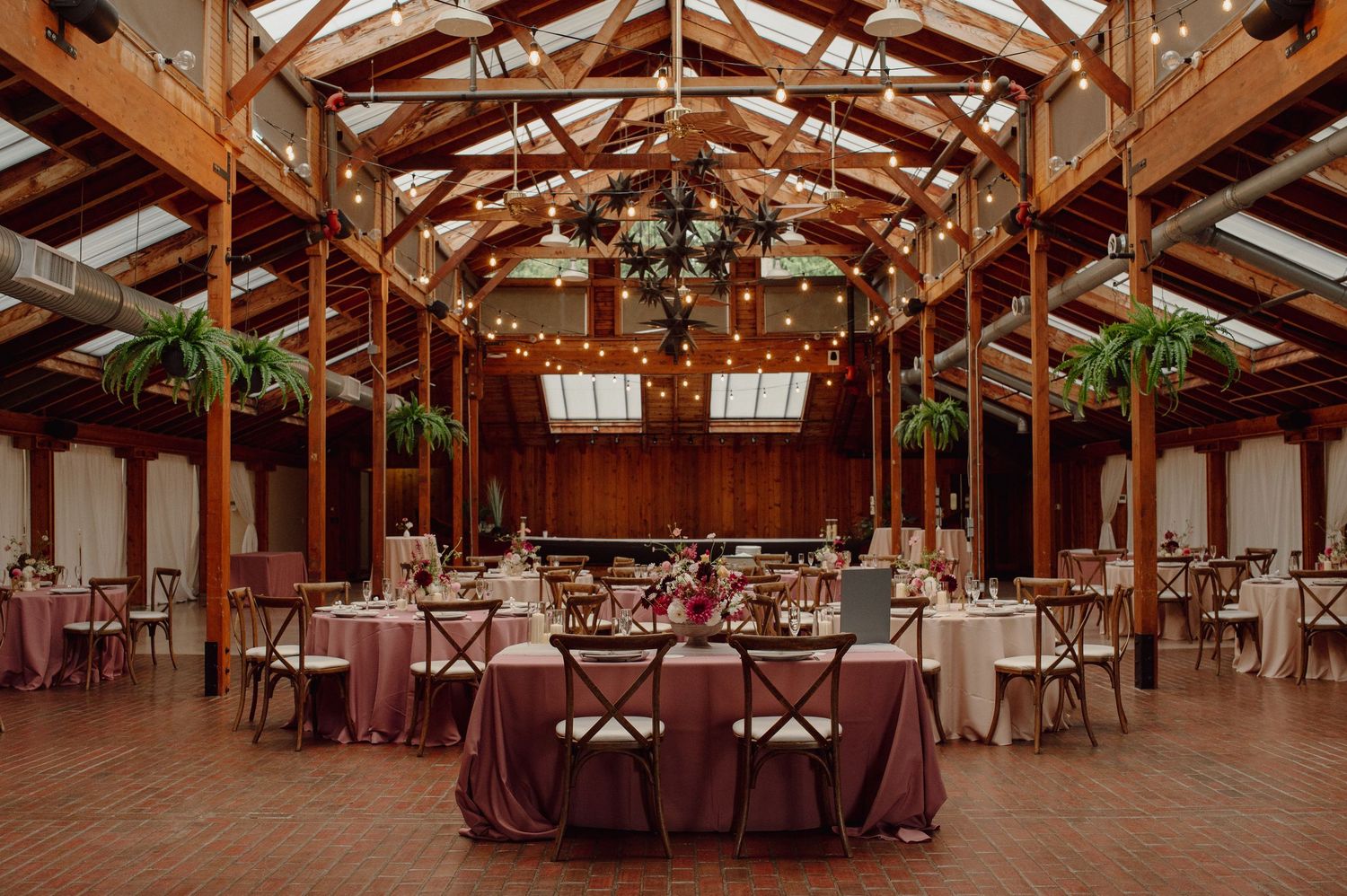 Large rustic wooden event venue with exposed beams and elegant table settings for a wedding reception.