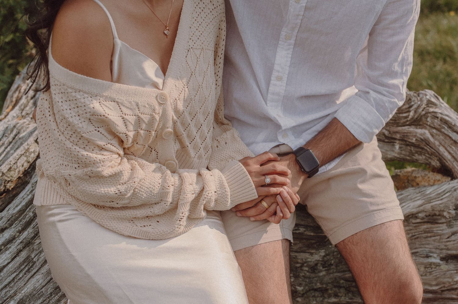 Close-up detail of two people holding hands while sitting together outdoors.