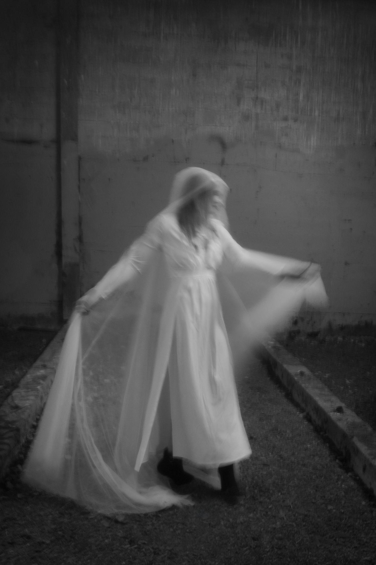 A sequence of black and white photos showing an ethereal figure in flowing white fabric moving gracefully against a dark wall.