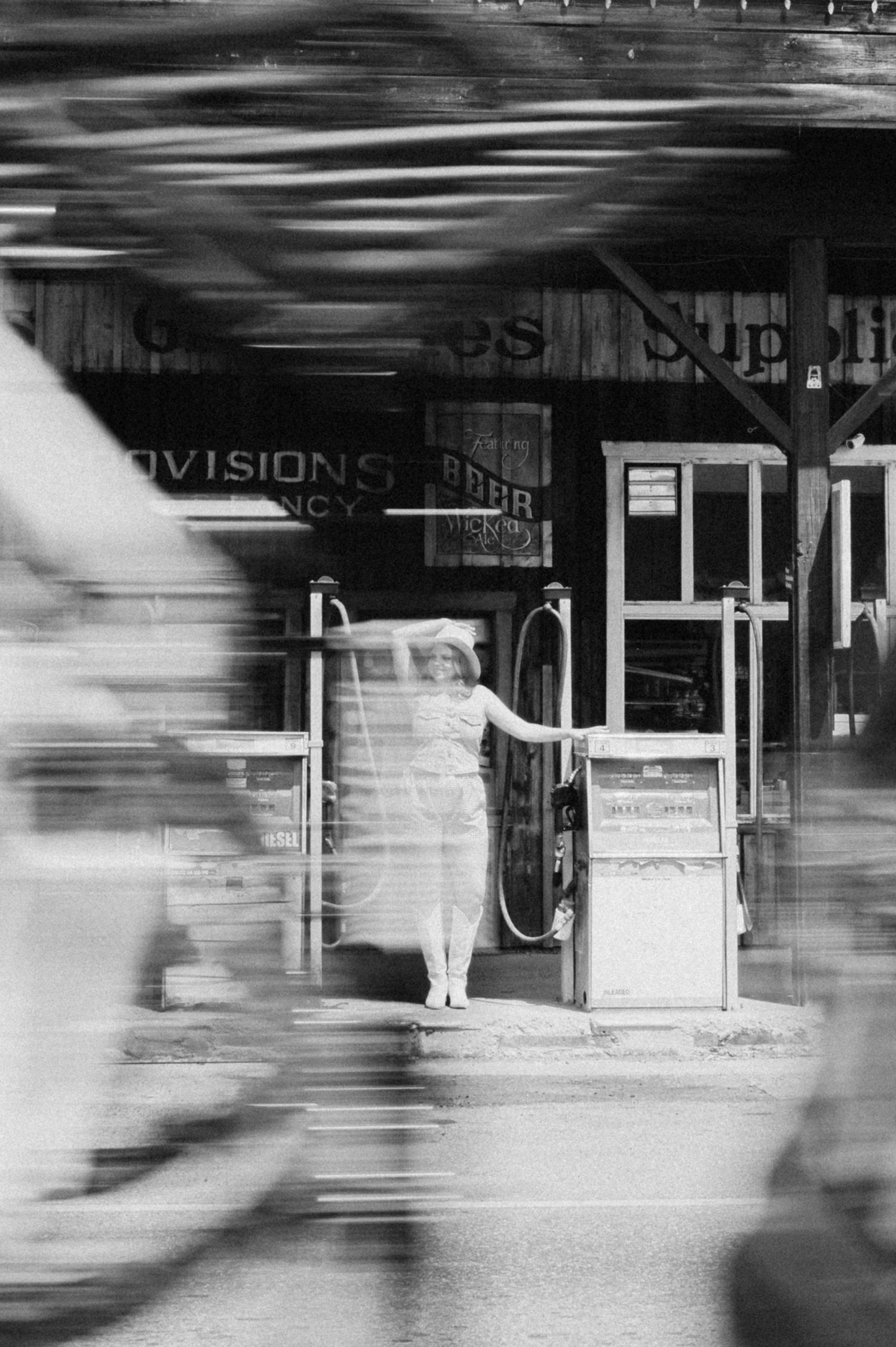 Motion blur black and white photograph shows figures walking past storefronts creating an abstract urban scene.