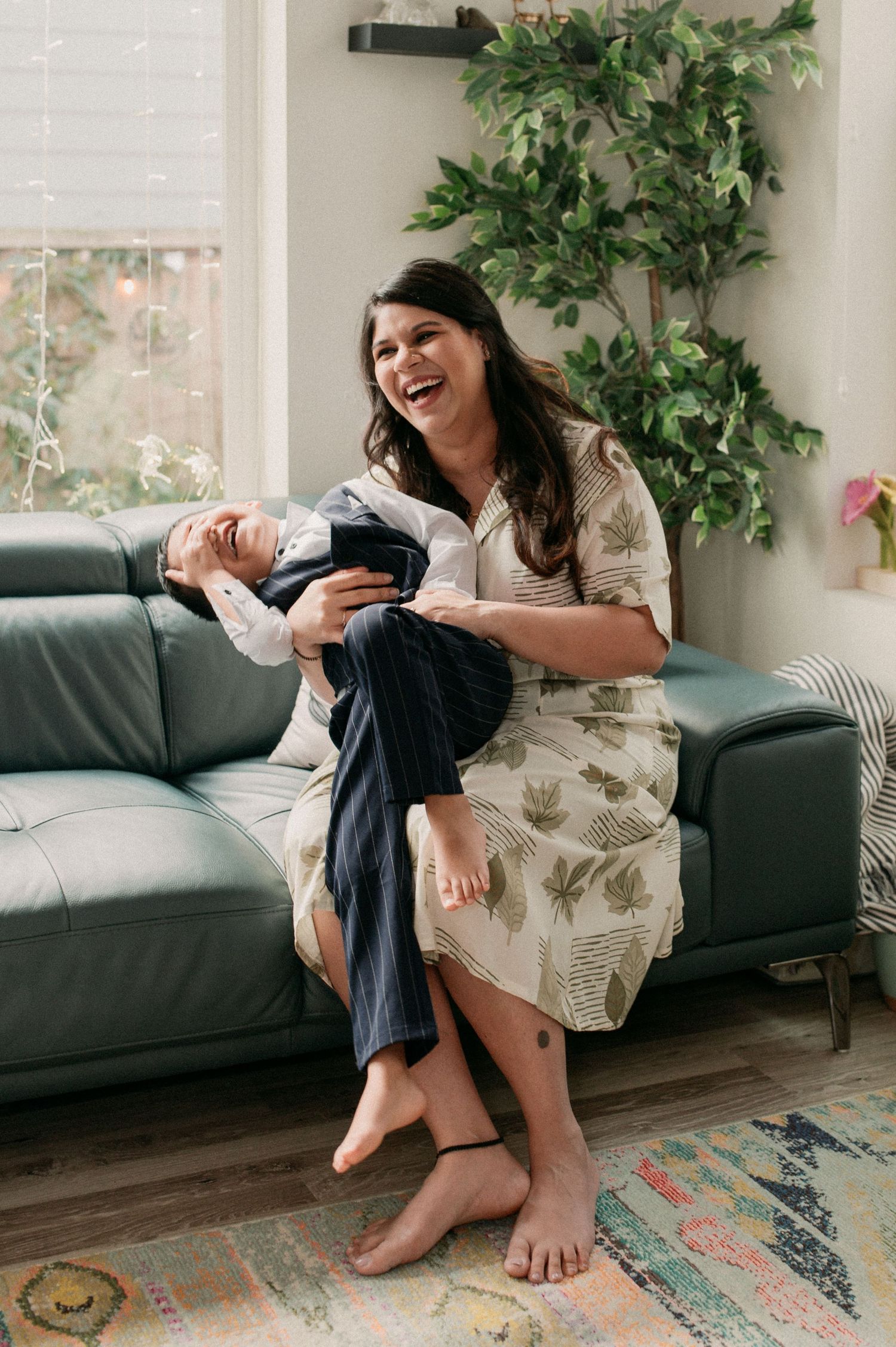 A heartwarming moment of laughter shared on a dark teal couch with houseplants in the background.