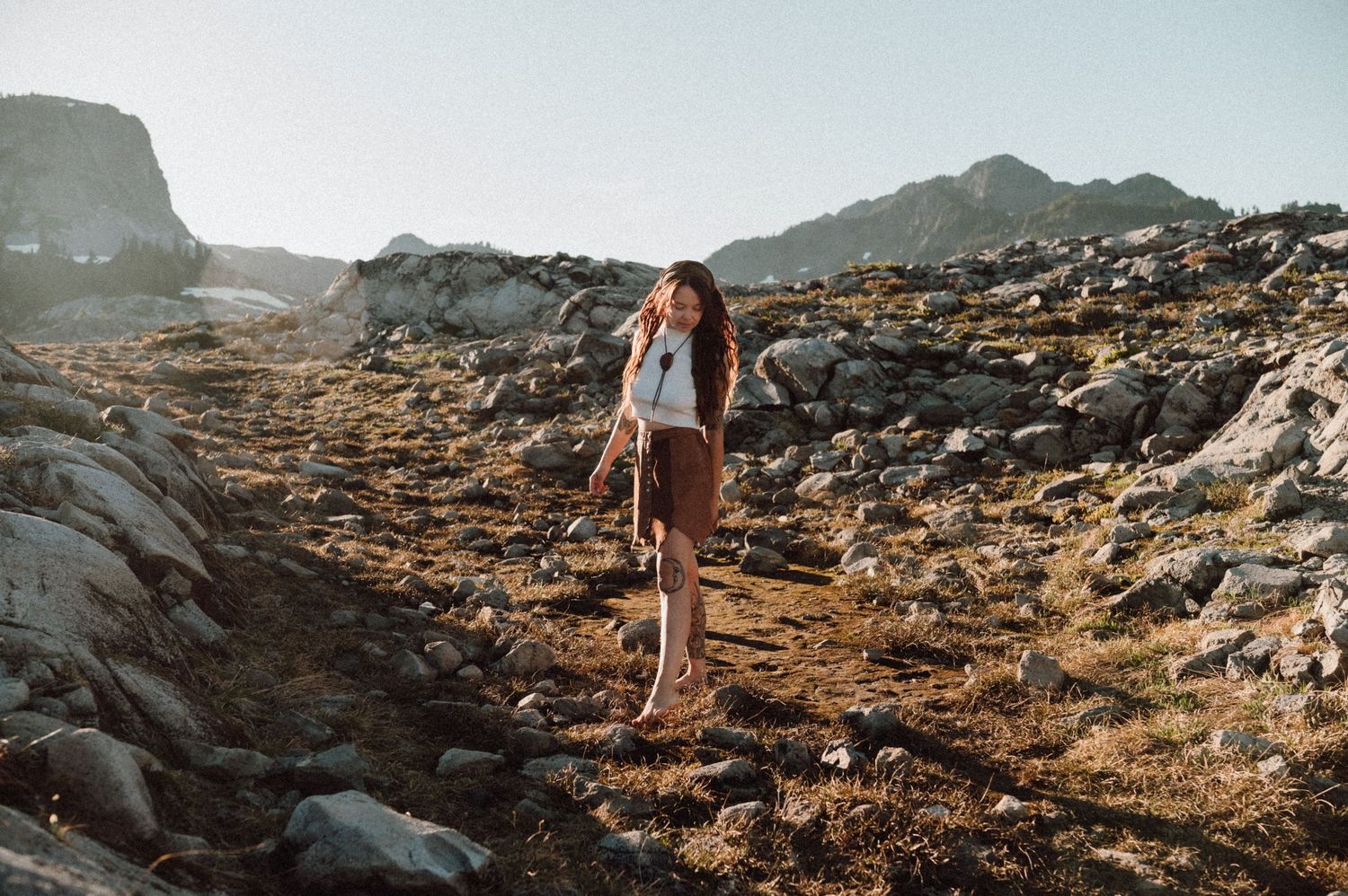 Hiker explores rocky mountain terrain at sunset with dramatic shadows and golden lighting along a rugged trail.