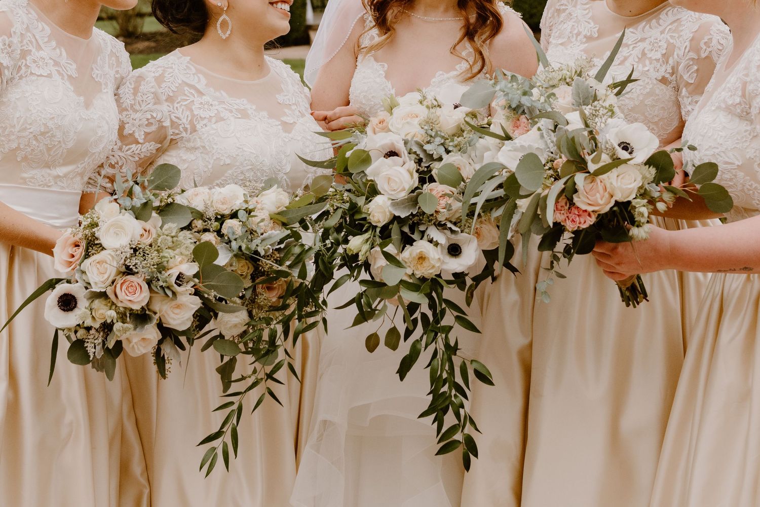 Elegant white and green wedding bouquets held against cream-colored bridesmaid dresses.