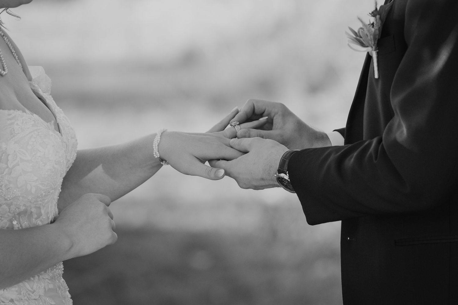 Black and white photo of hands exchanging wedding rings during a marriage ceremony.