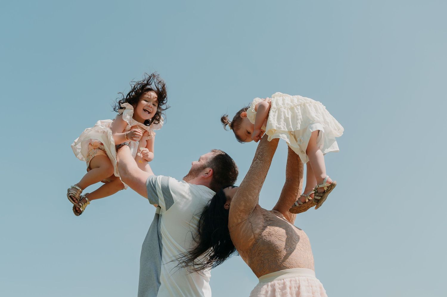 A joyful family plays together outdoors against a blue sky on a sunny day.