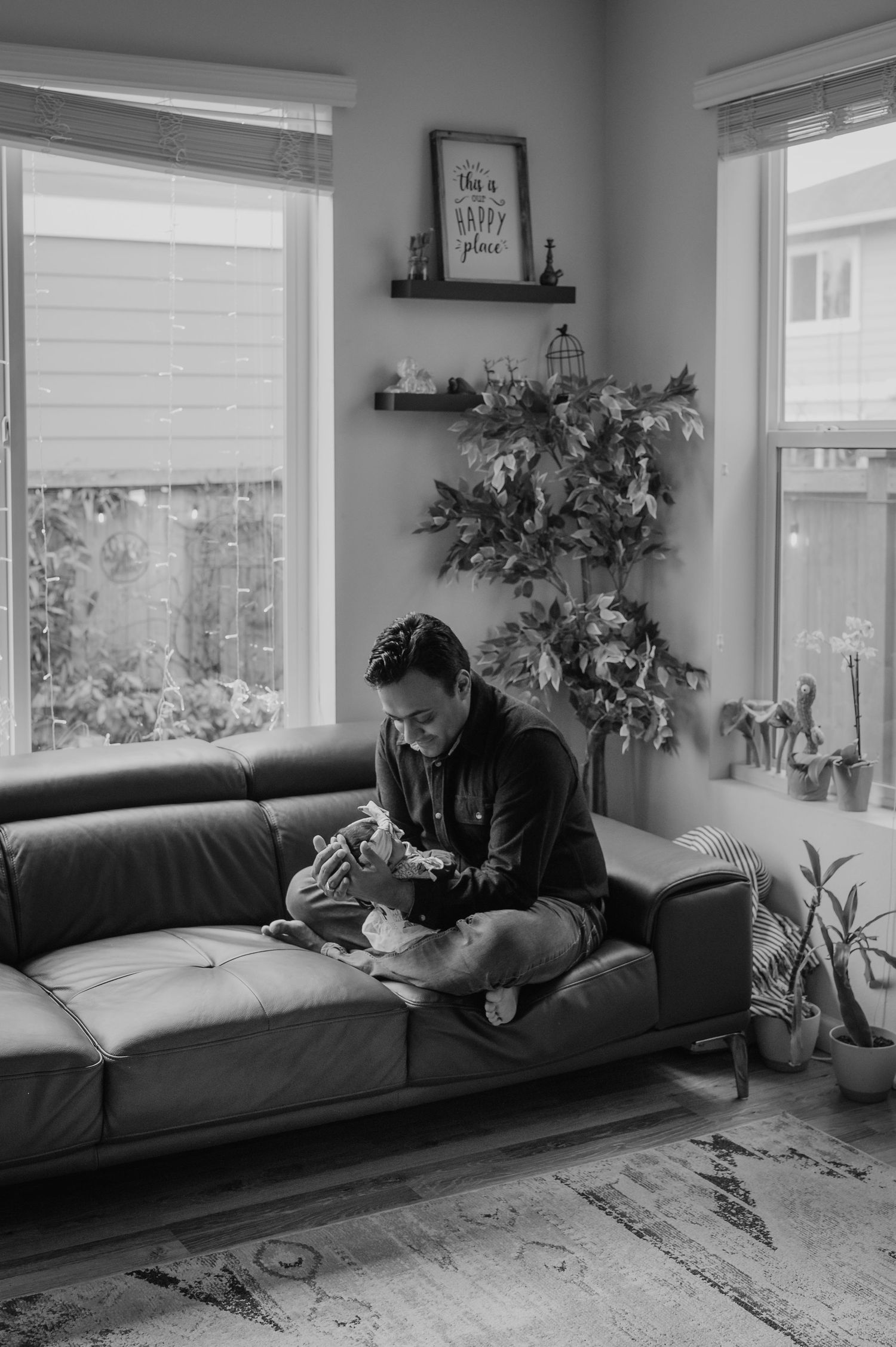 A cozy living room scene with someone relaxing on a grey couch surrounded by plants and natural light.