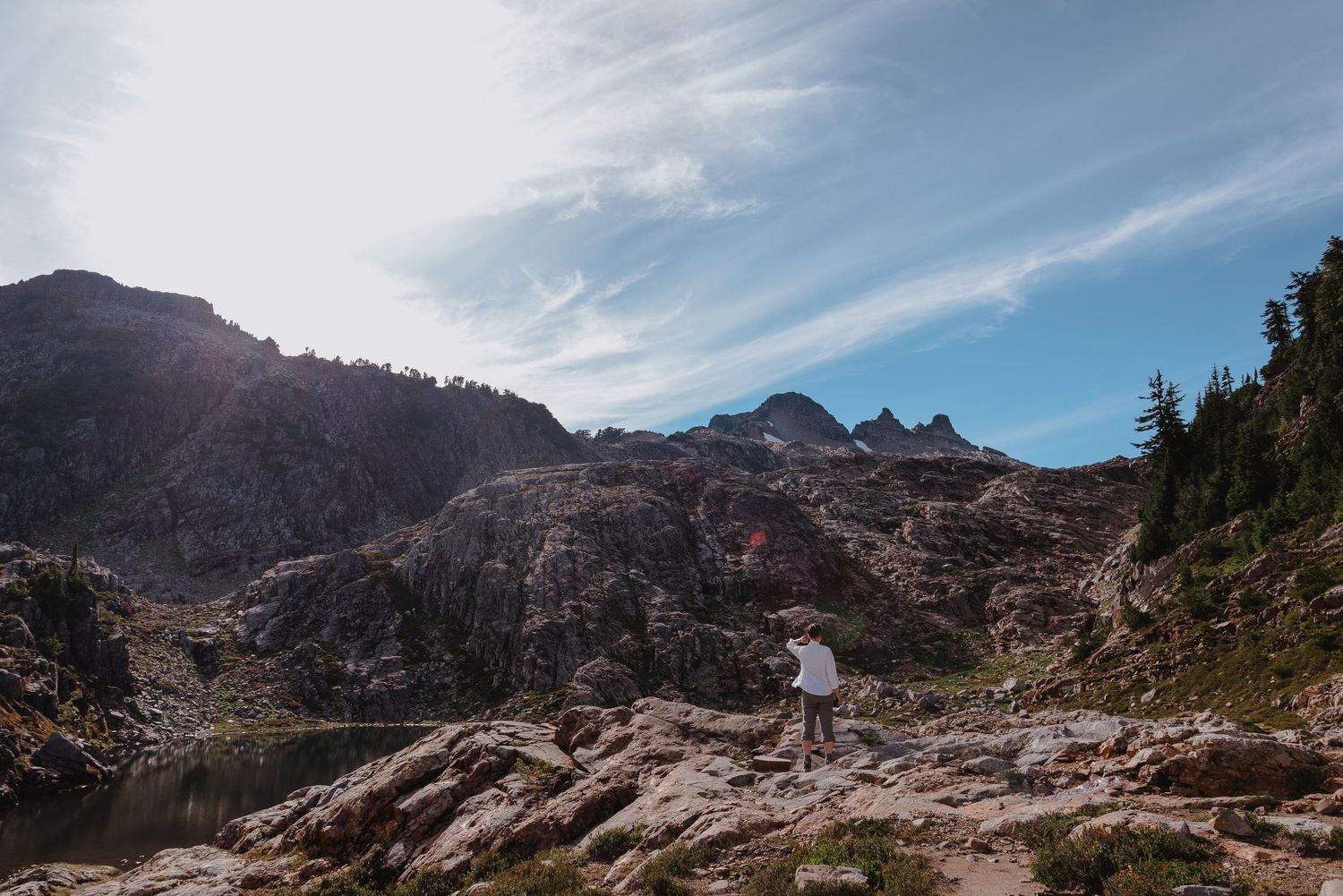 A panoramic mountain landscape with rocky peaks, evergreen trees, and dramatic clouds stretching across the horizon.