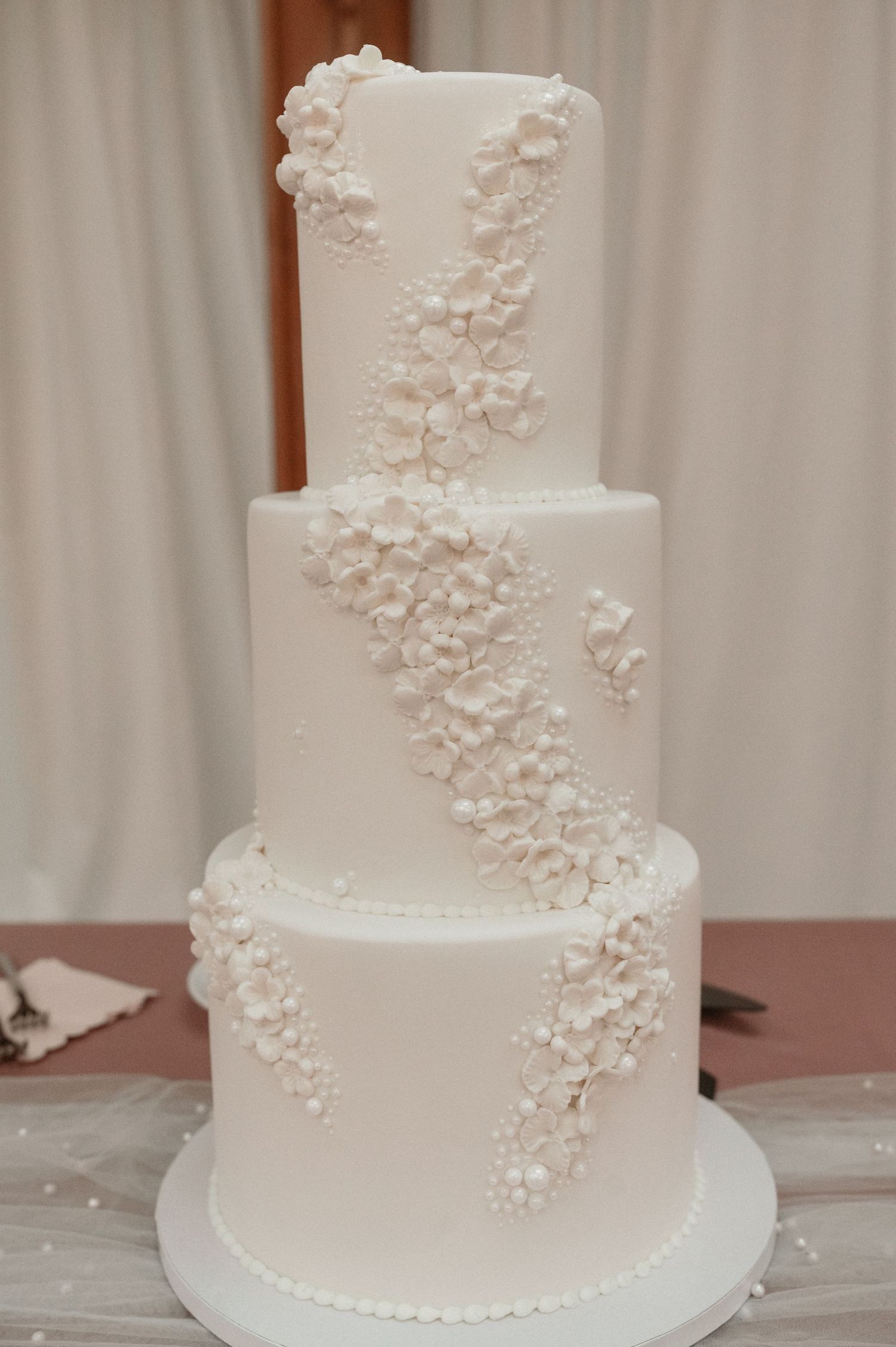Elegant three-tier white wedding cake decorated with delicate floral appliques cascading down the sides.