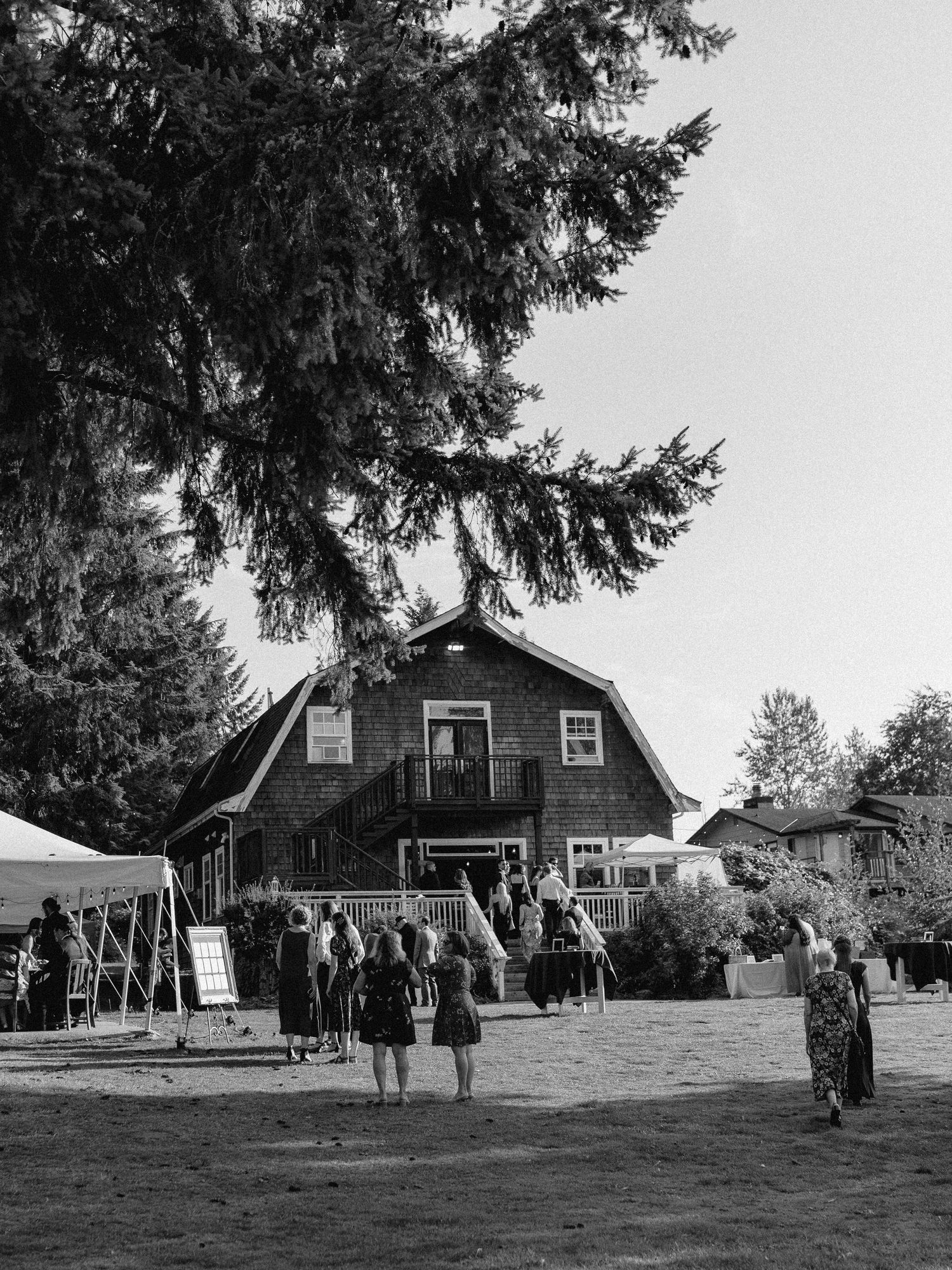A black and white photo of a rustic barn wedding venue with guests gathering outside.
