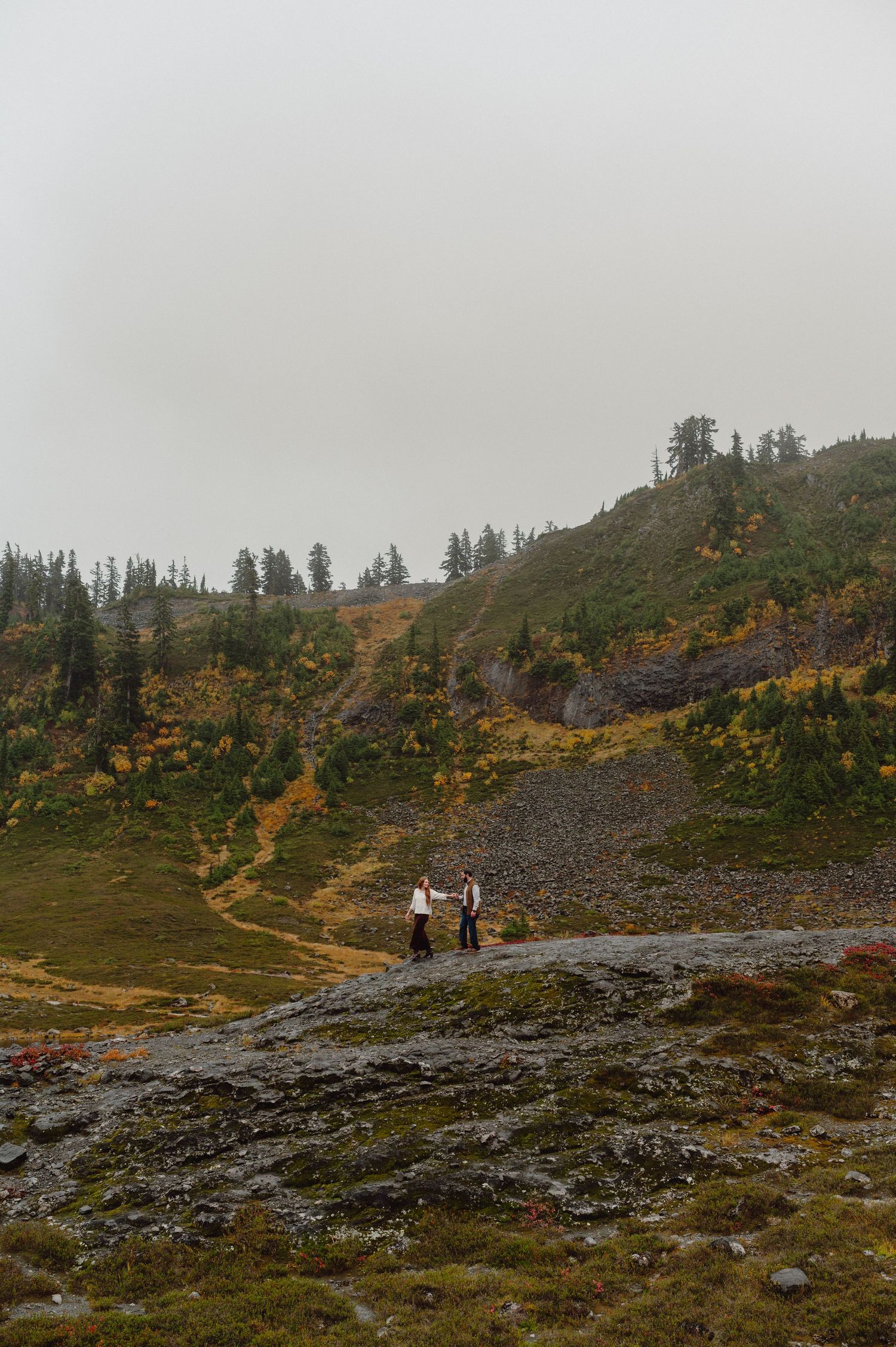 Hikers traverse a misty mountain trail surrounded by autumn foliage and evergreen trees in the Pacific Northwest.
