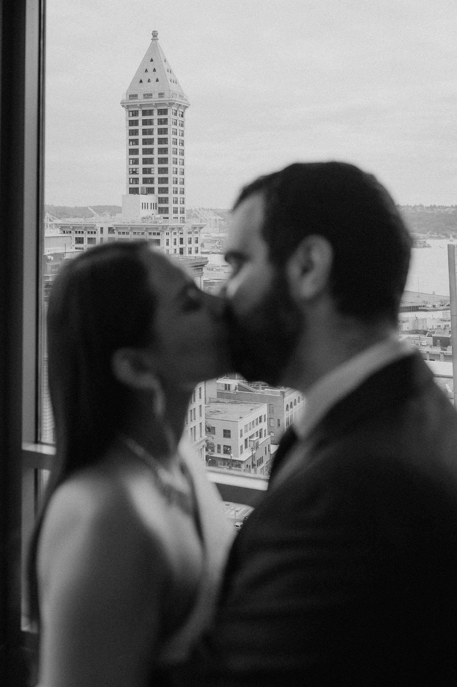 A romantic silhouette of a couple sharing a kiss against a cityscape backdrop with tall buildings visible through windows.