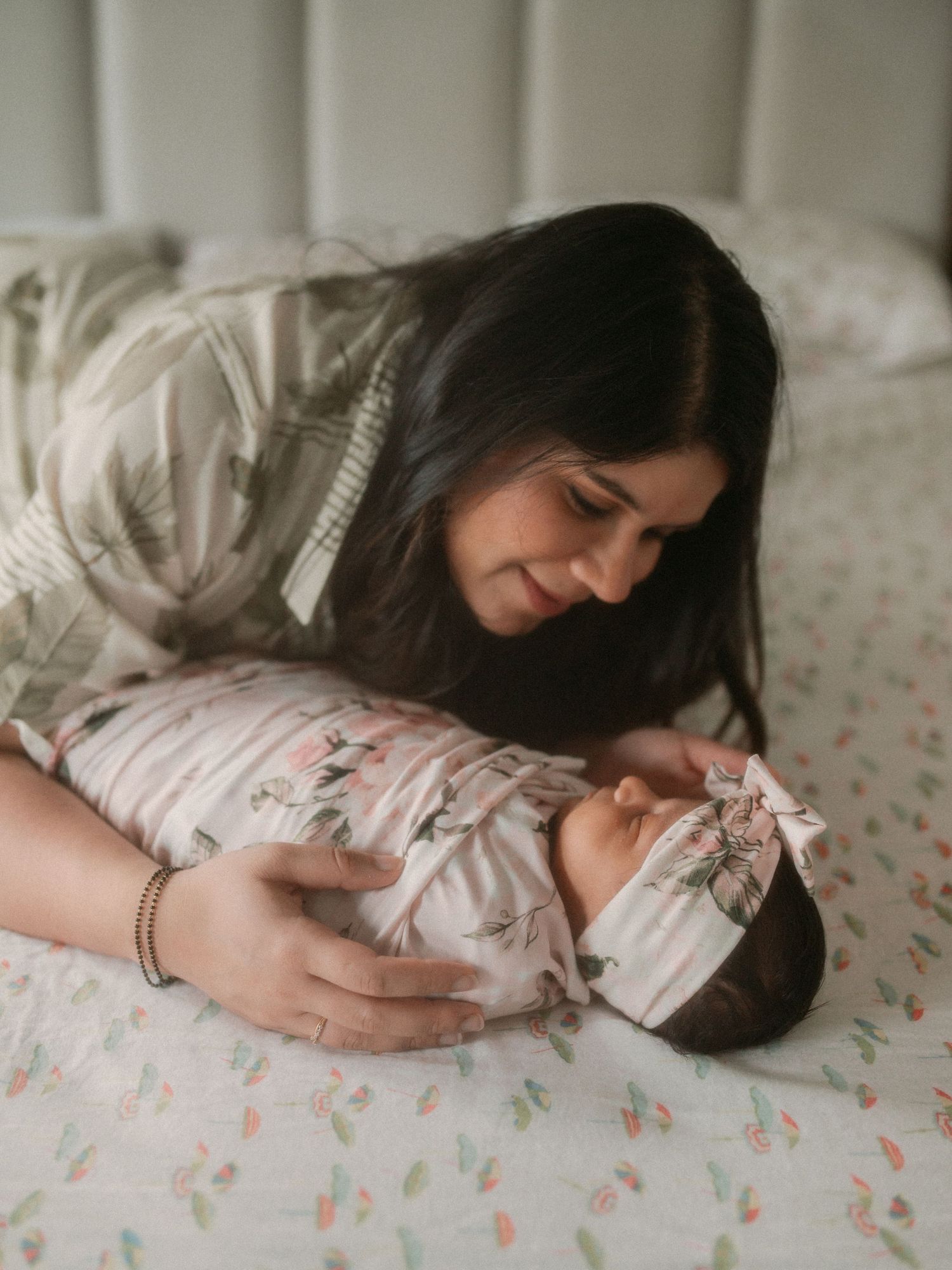 A tender moment between parent and newborn baby lying together on a floral patterned bed.