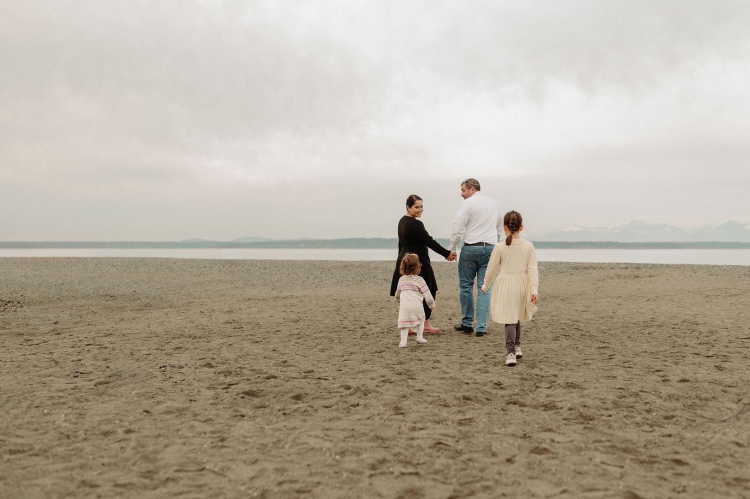 Family walking together on a cloudy beach with water in the background.