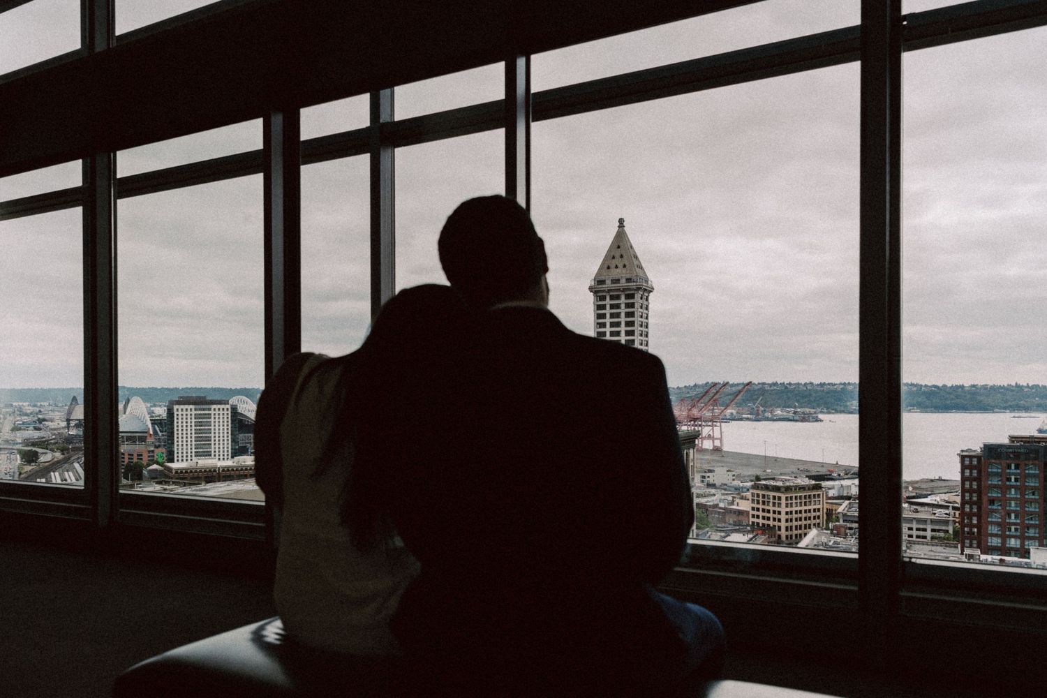 Silhouetted figures look out large windows at a cityscape with the US Capitol dome visible in the distance.