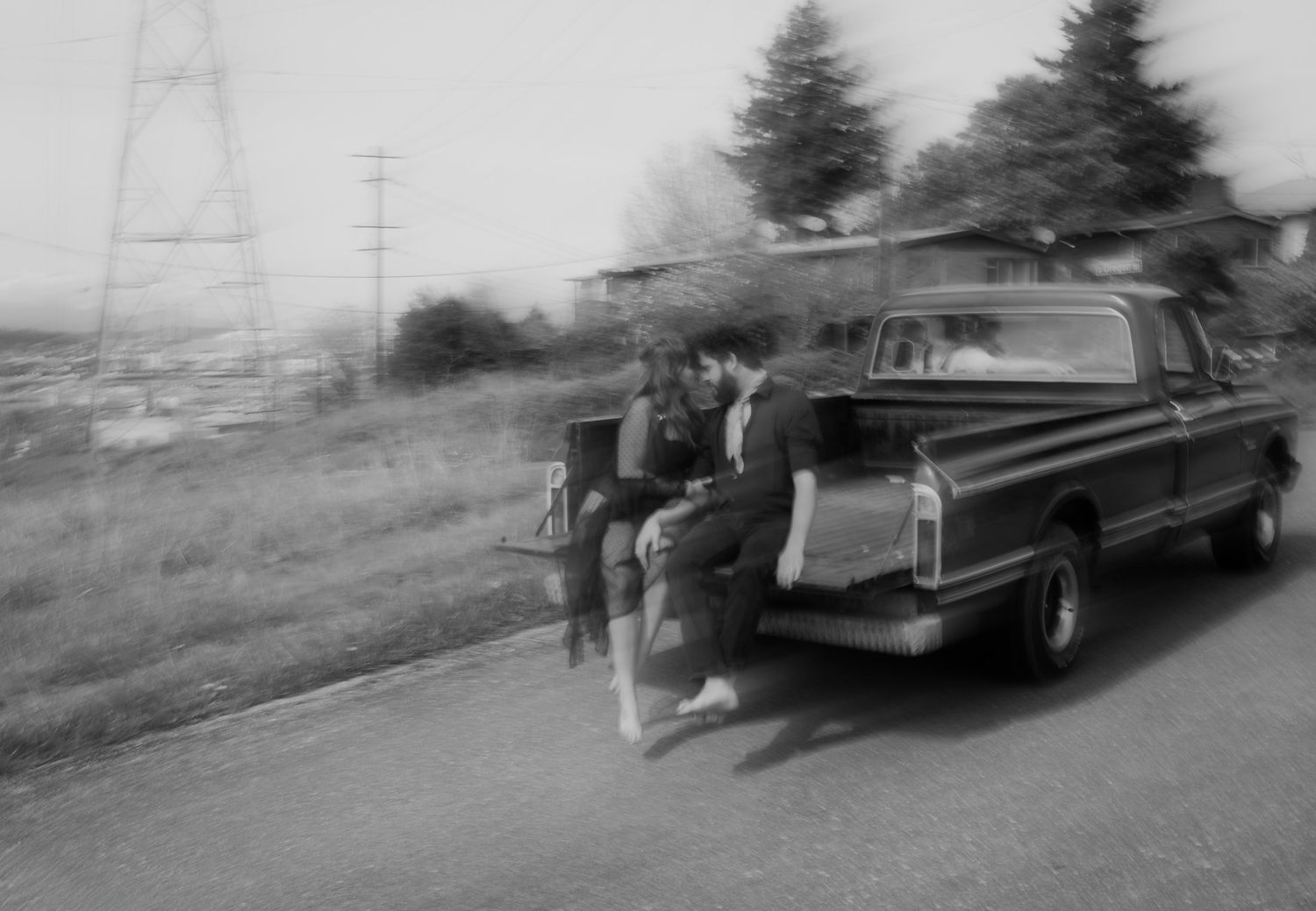 A vintage black and white photograph showing people standing next to a classic car on a hillside road.