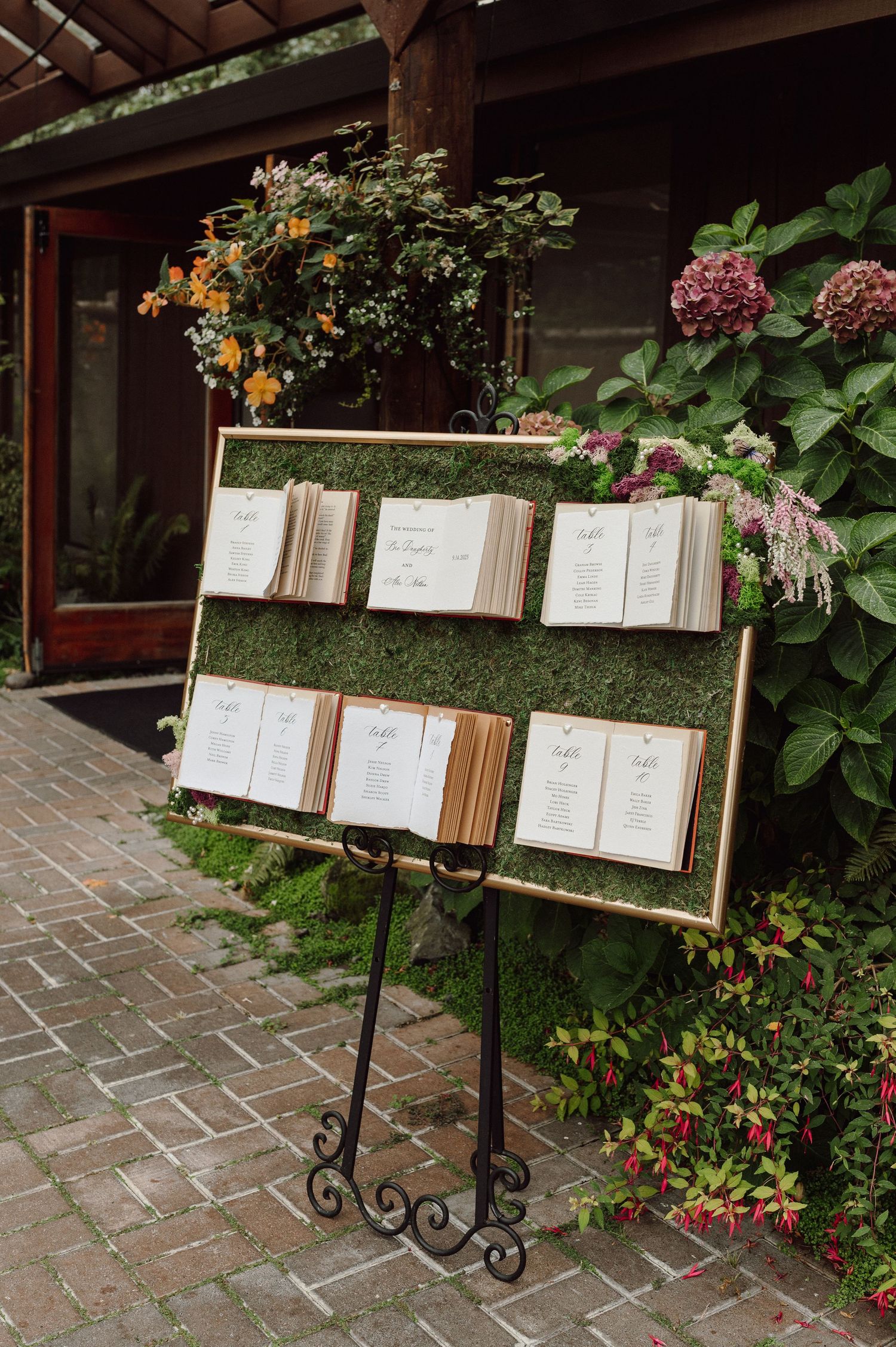 Rustic menu stands with wooden frames displayed along a garden path with colorful flowers and brick pavers.