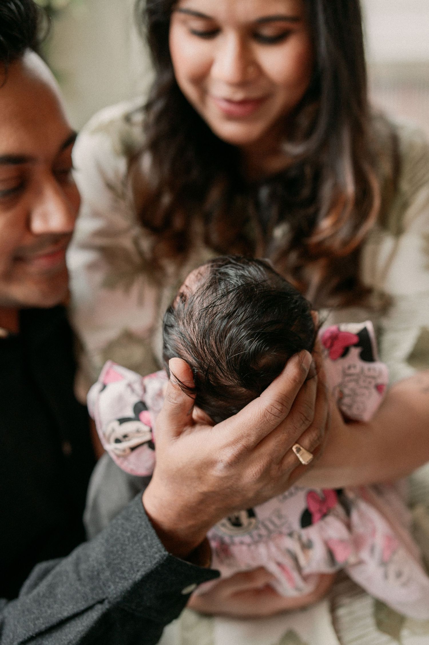 A tender moment as parents cradle their newborn baby wearing a floral dress in an intimate indoor setting.