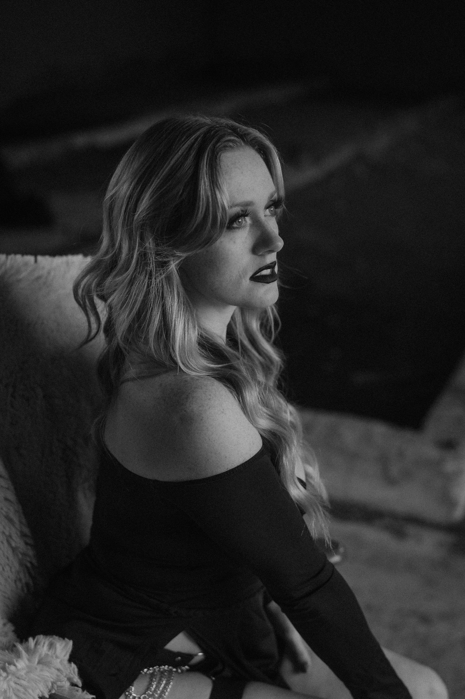Dramatic black and white portrait of a woman with wavy blonde hair in an off-shoulder top looking to the side.