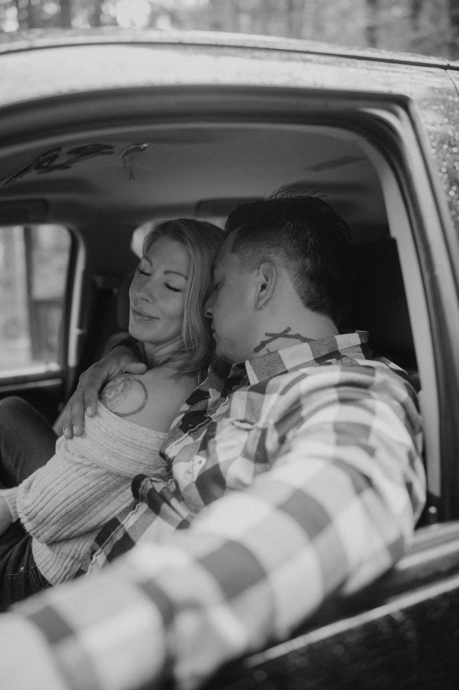 A romantic black and white photograph of a couple sitting close together inside a vintage car.