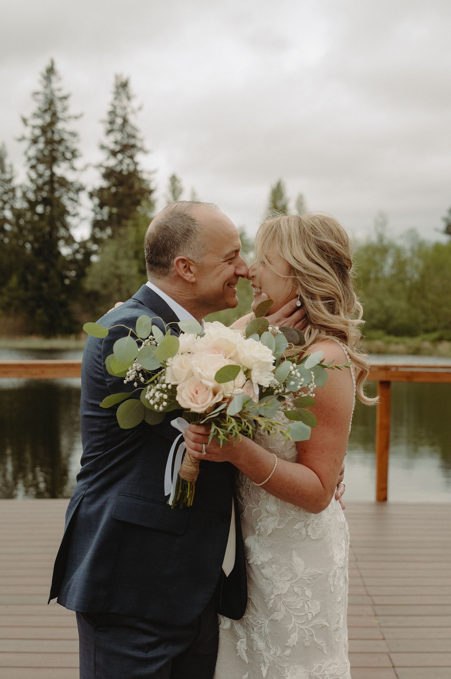 Joyful wedding couple sharing an intimate moment on a deck overlooking a serene lake.
