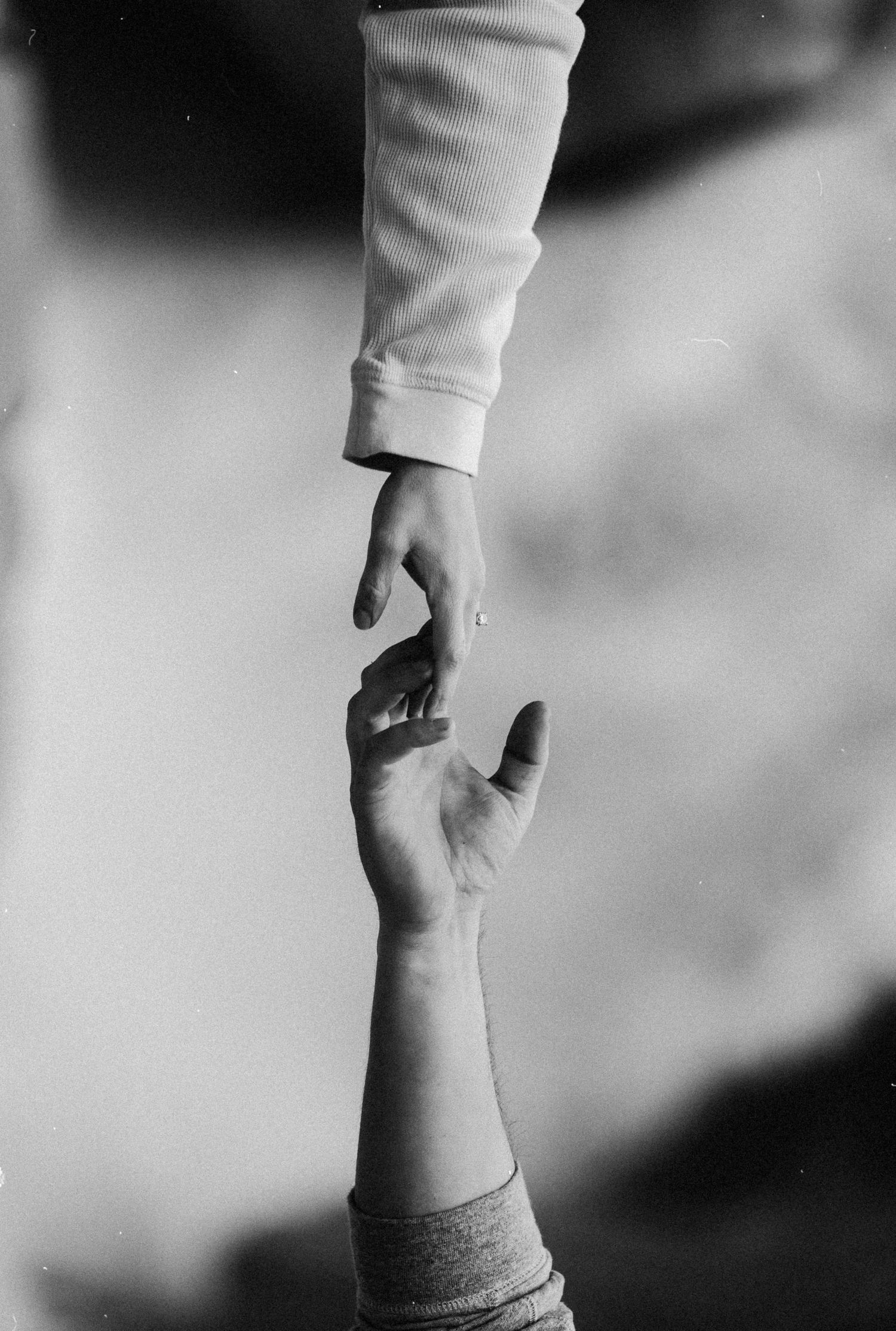 Black and white image of two hands reaching out to hold each other against a blurred background.