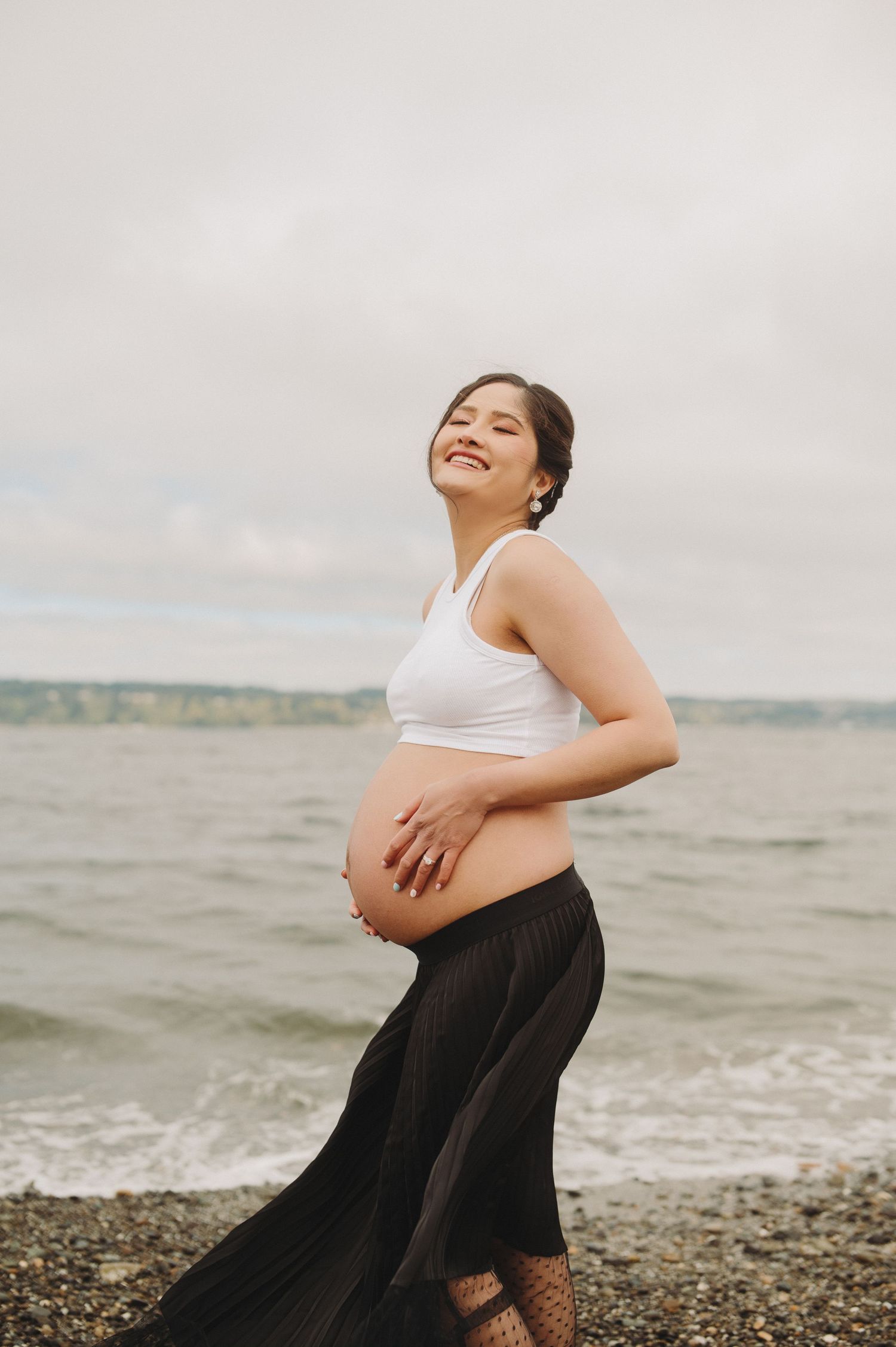 Joyful maternity portrait by the beach with waves in background.