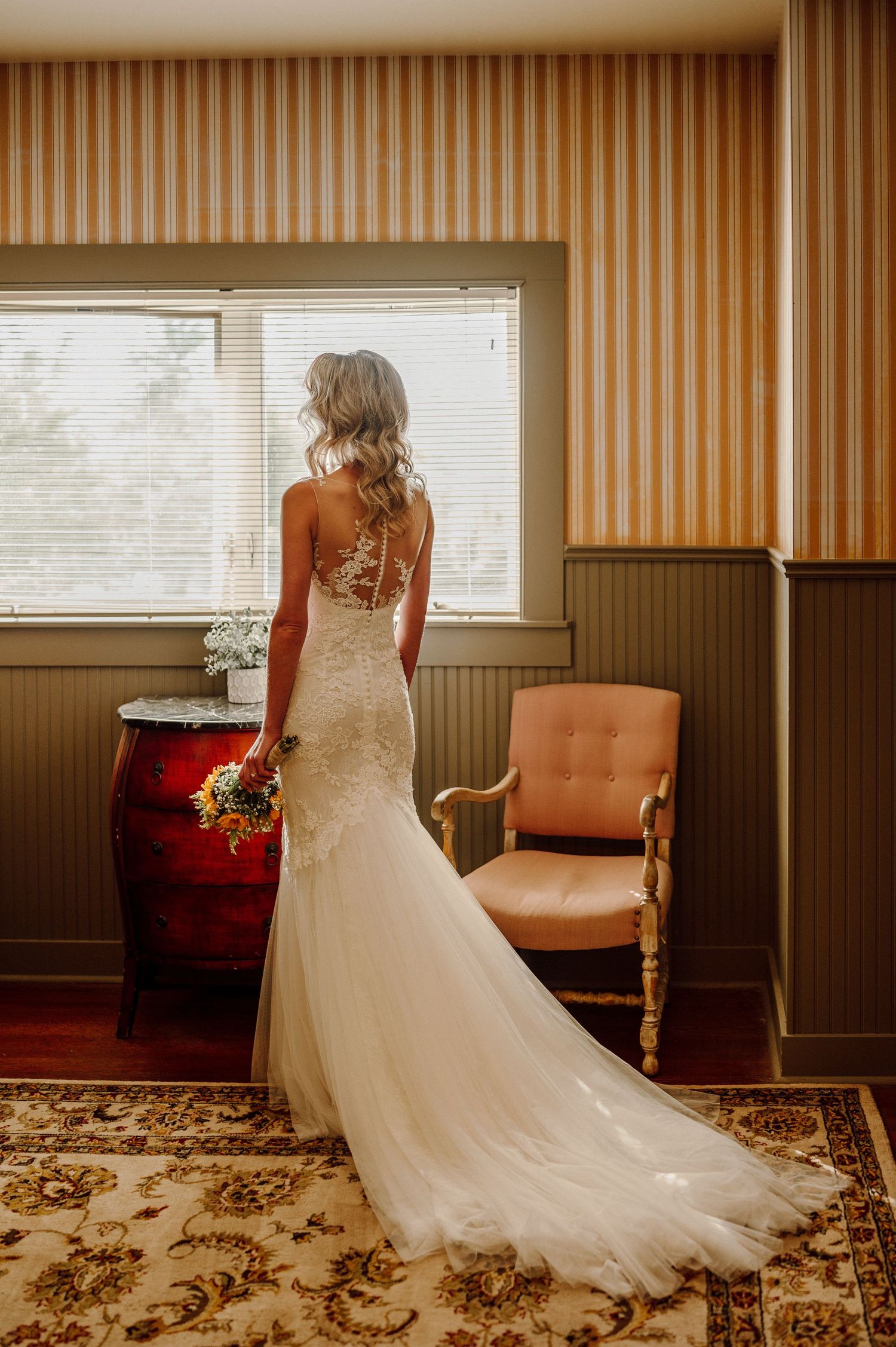 Elegant lace wedding dress with train displayed in a room with striped wallpaper.
