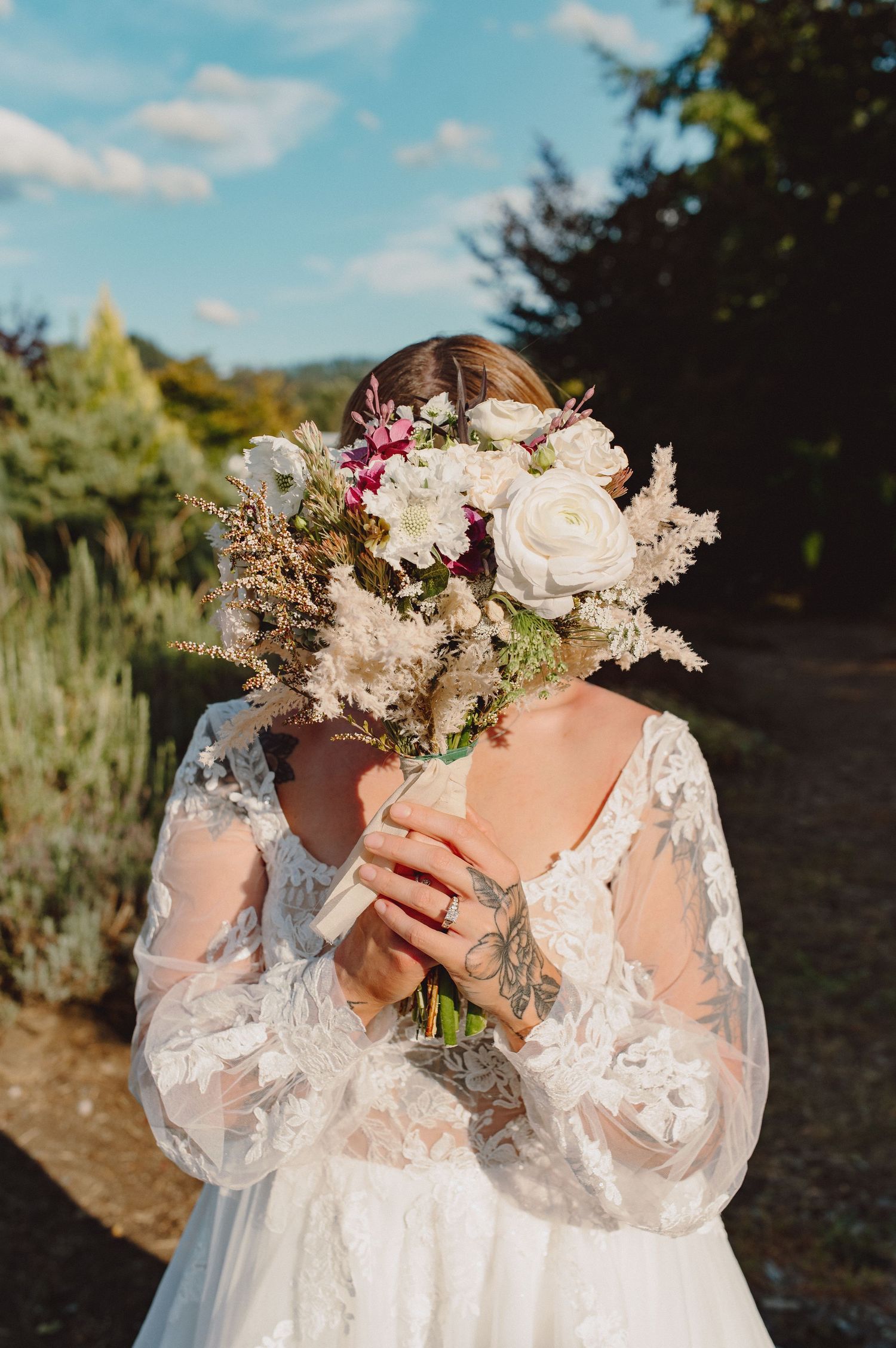 Beautiful bridal bouquet with white roses and delicate dried flowers held by someone in a lace wedding dress.