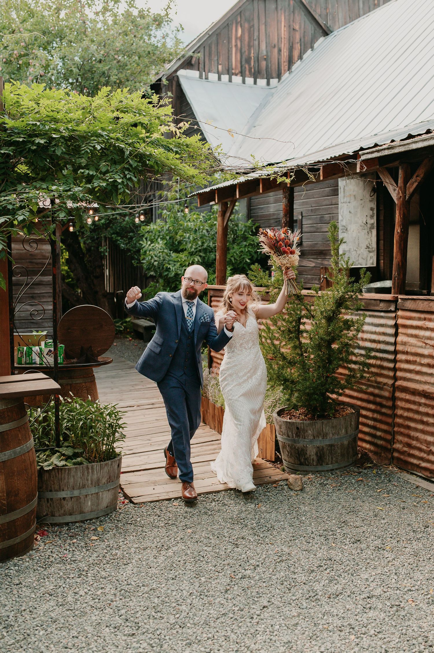 Joyful newlyweds celebrate while walking outside a rustic barn venue.