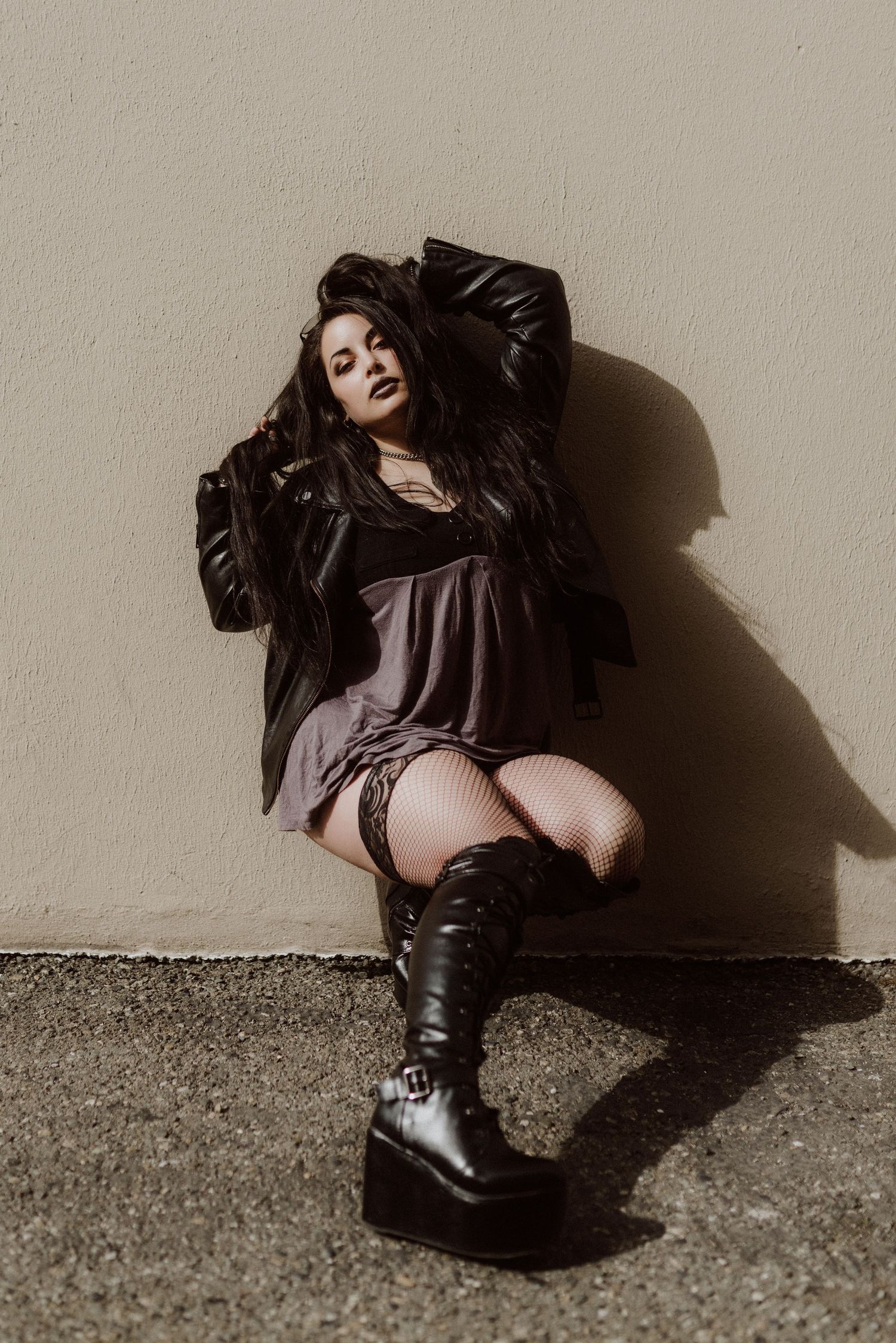 A dramatic black and white fashion photo series showing a figure in dark clothing and boots against a light wall.
