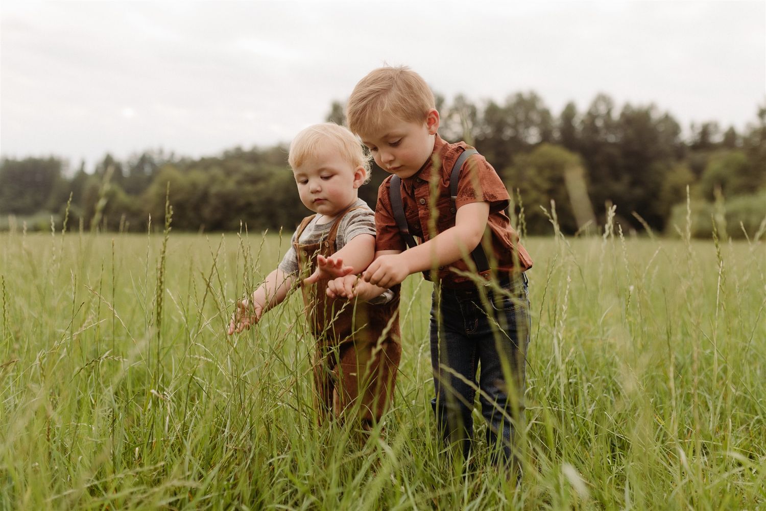 Two children explore together in tall grass on a sunny summer day.
