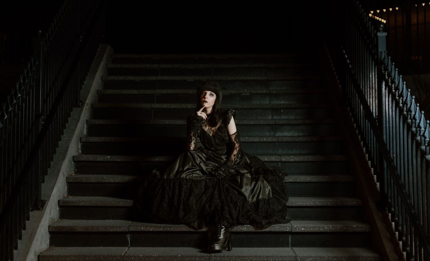 A dark and moody scene of someone sitting alone on concrete steps in dramatic lighting.