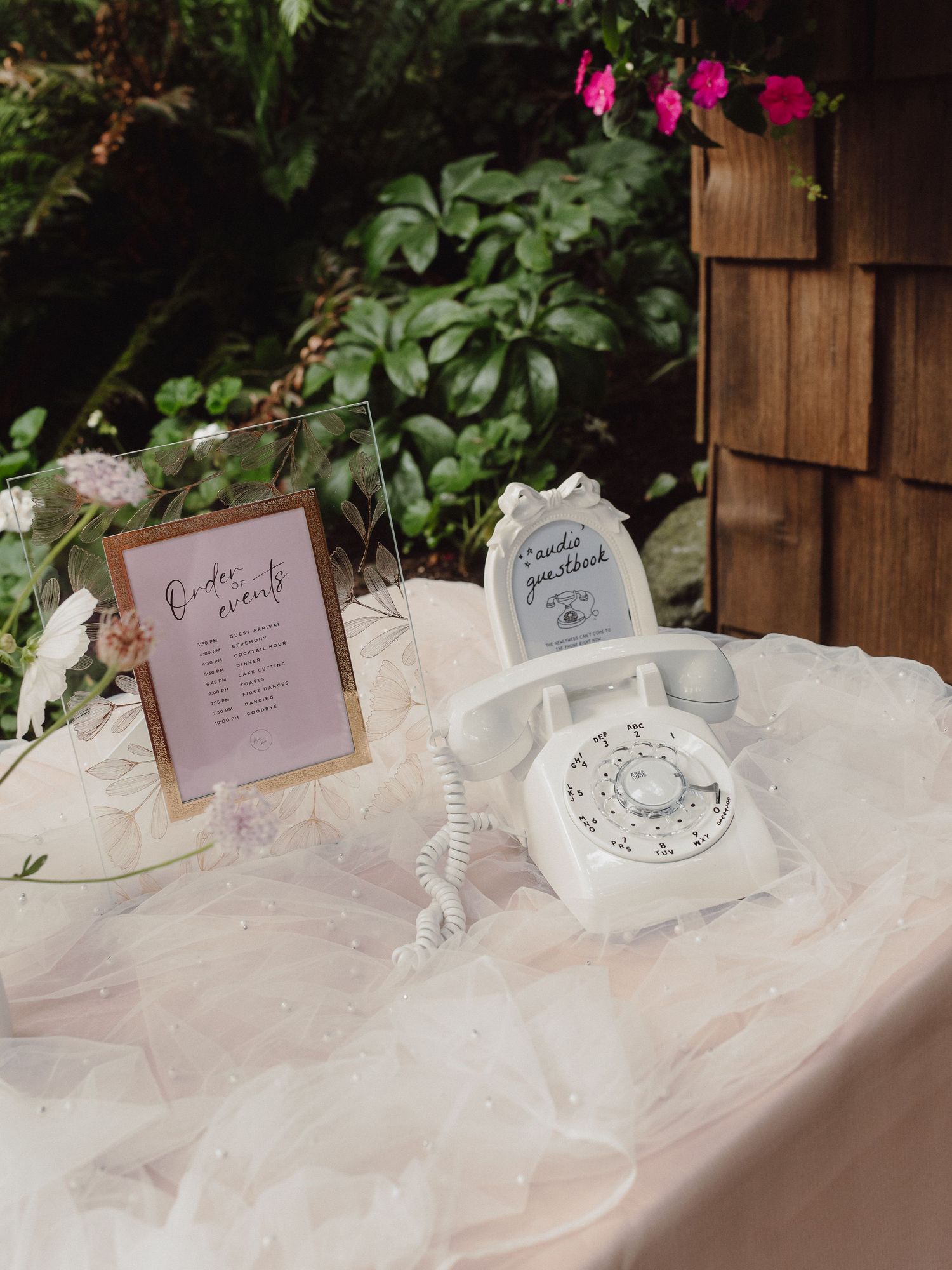 Vintage white rotary telephone displayed on delicate lace tablecloth with decorative wedding signage in garden setting.