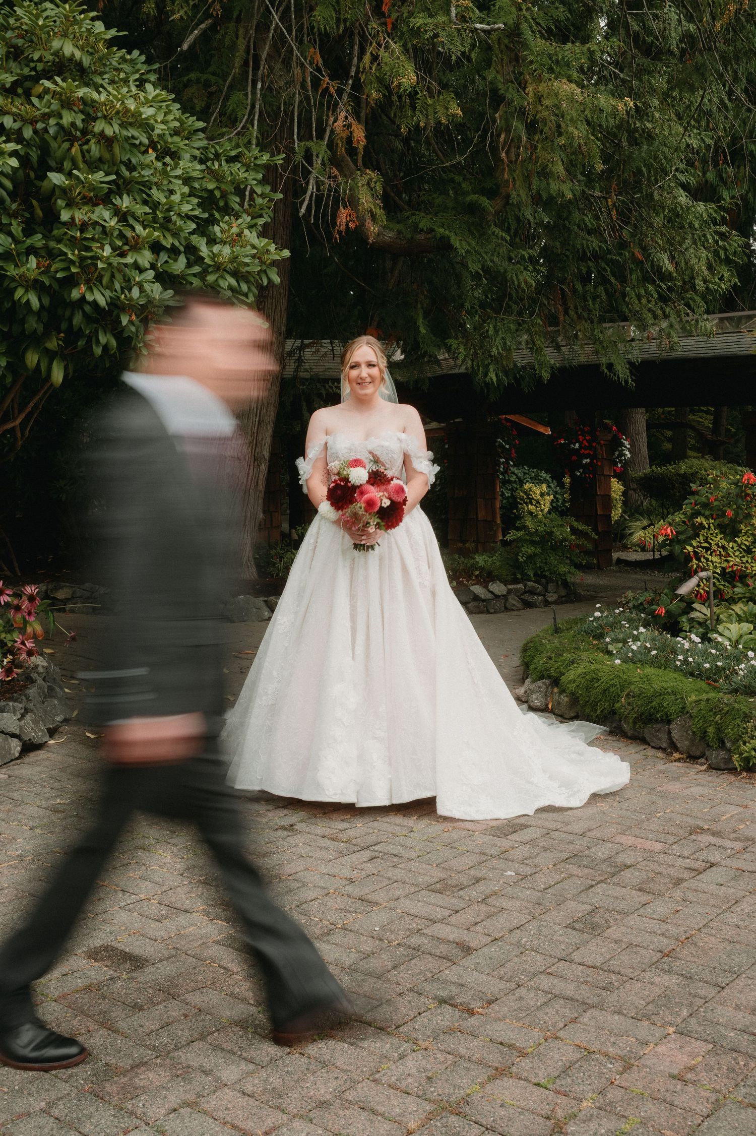 Motion blur imagery captures walking figures passing by a wedding scene on a brick patio surrounded by lush gardens.