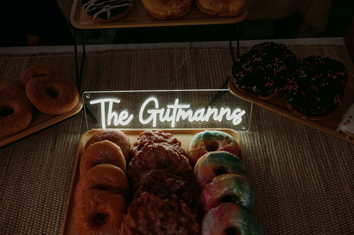 An arrangement of desserts and pastries displayed on wooden surfaces with neon signage illuminating the scene.