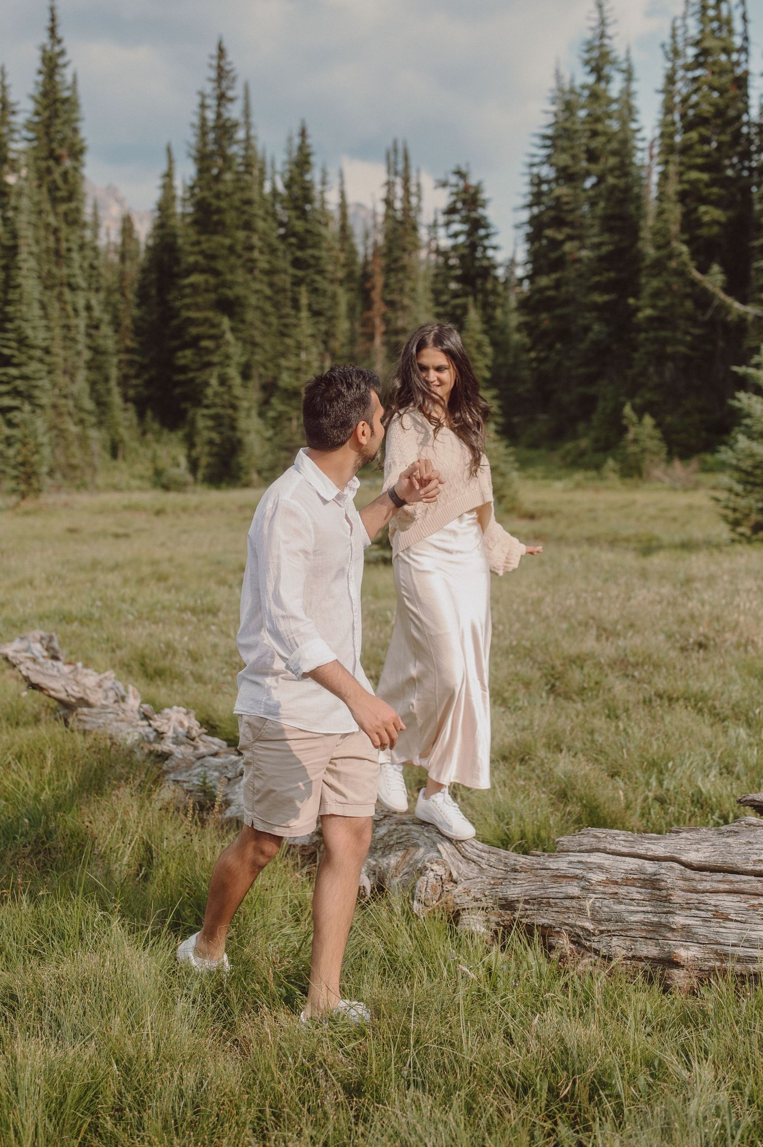 A couple standing in a mountain meadow surrounded by evergreen trees in romantic outdoor photoshoot.