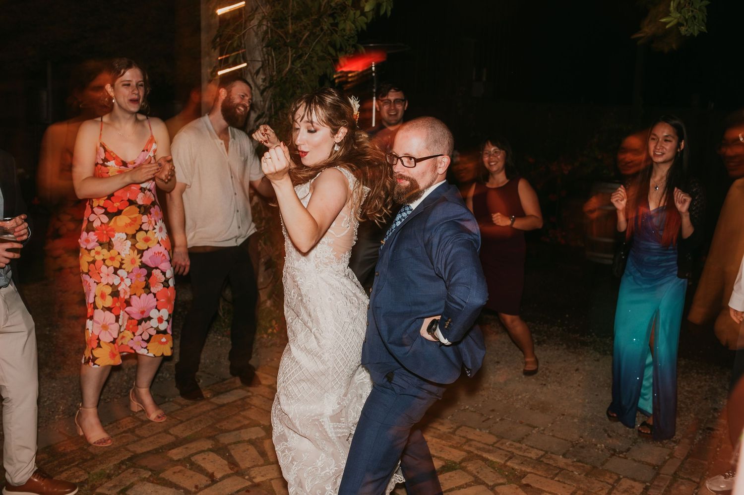 Lively wedding reception dancing scene at night with guests on a stone patio.