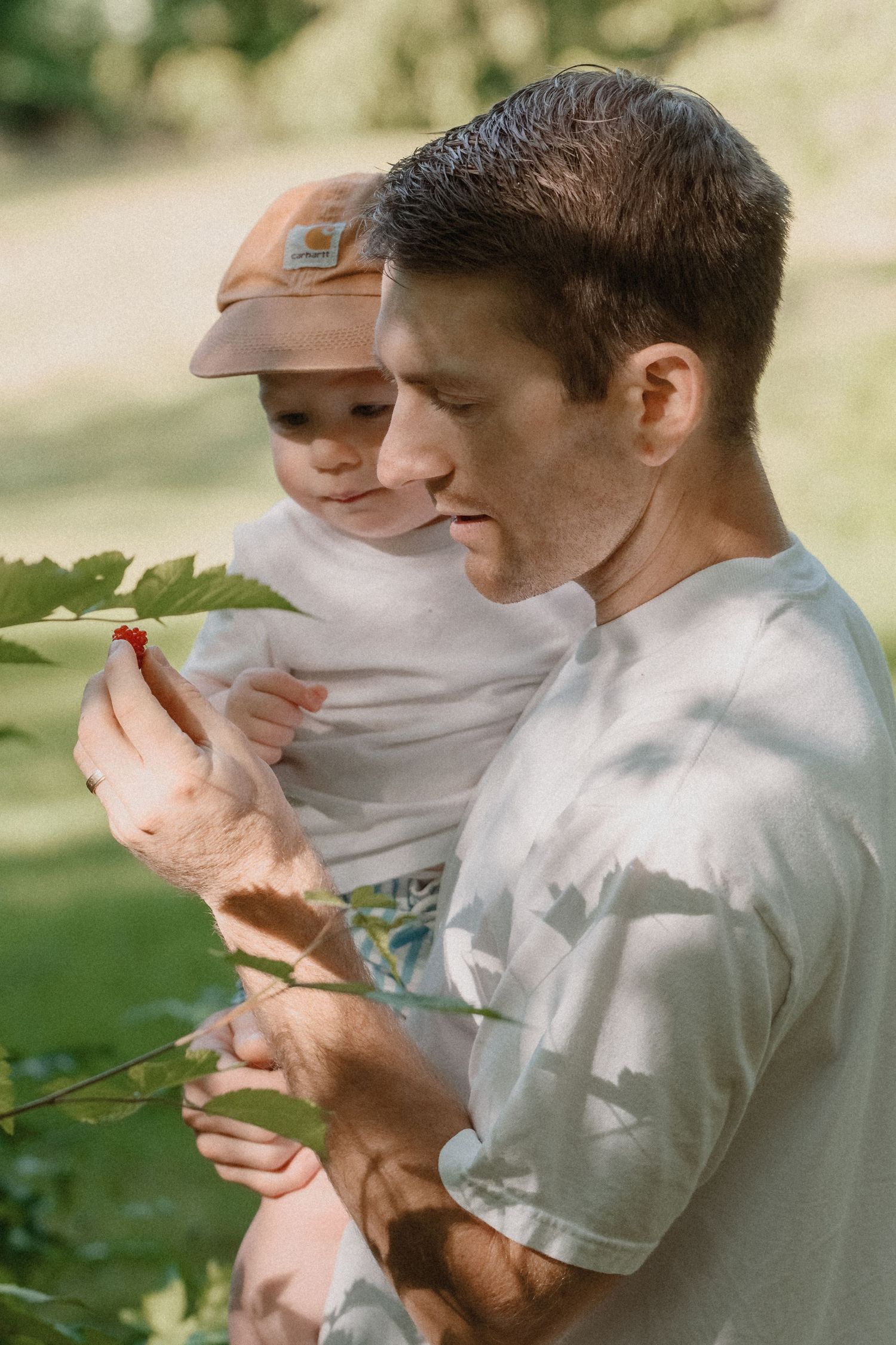 Two individuals in white shirts examining plant leaves outdoors in natural lighting.