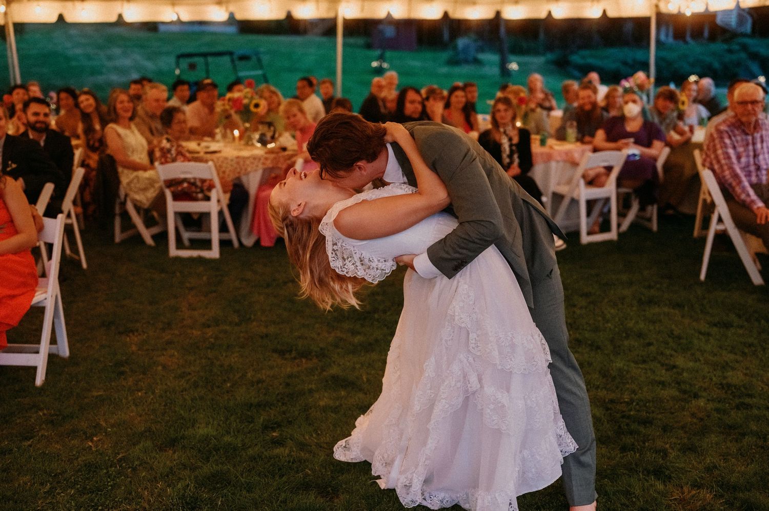 Wedding guests dancing joyfully together at an outdoor sunset reception on a grassy lawn.
