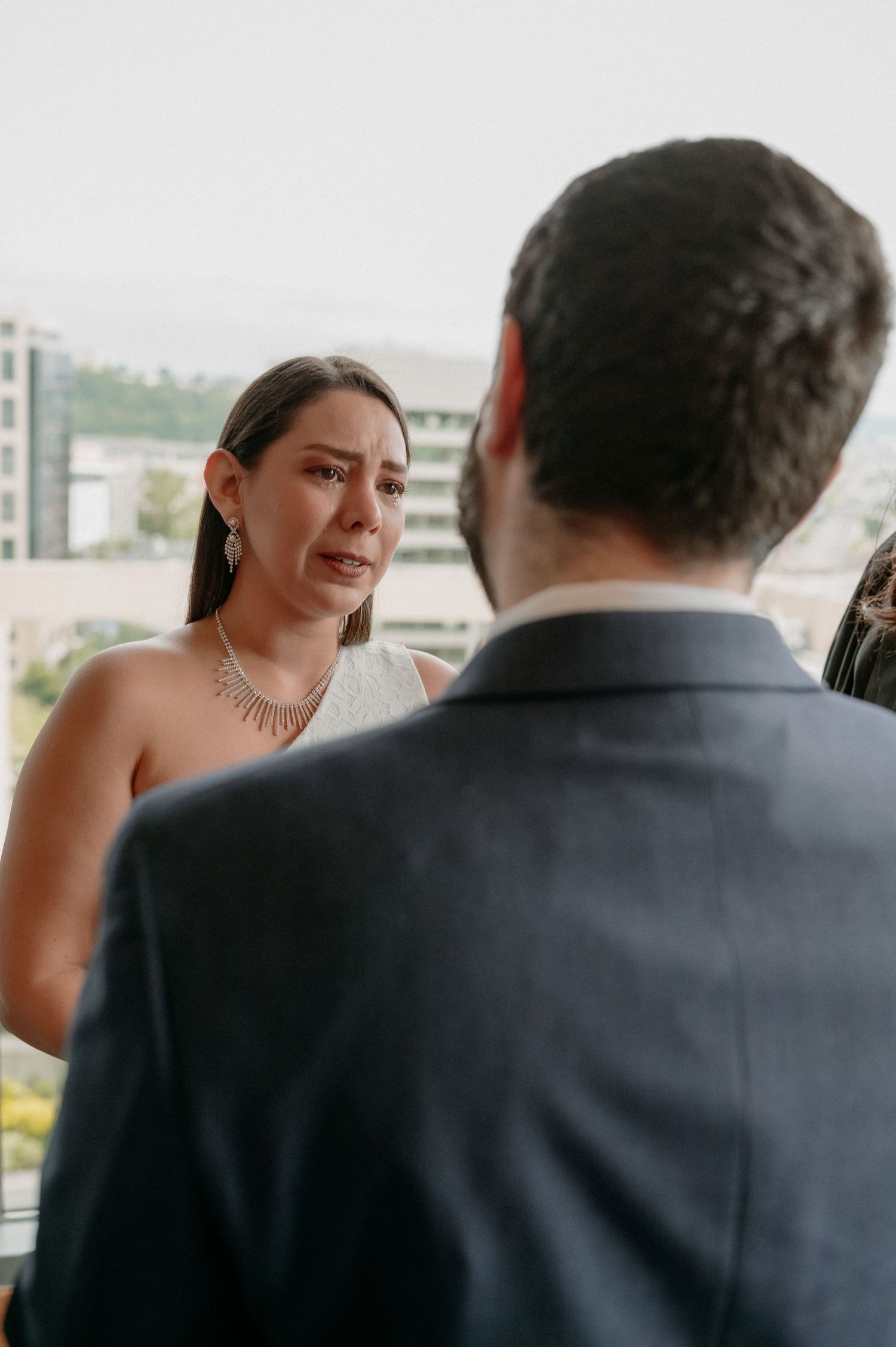 Couple shares an intimate moment during wedding ceremony on a balcony with city backdrop.