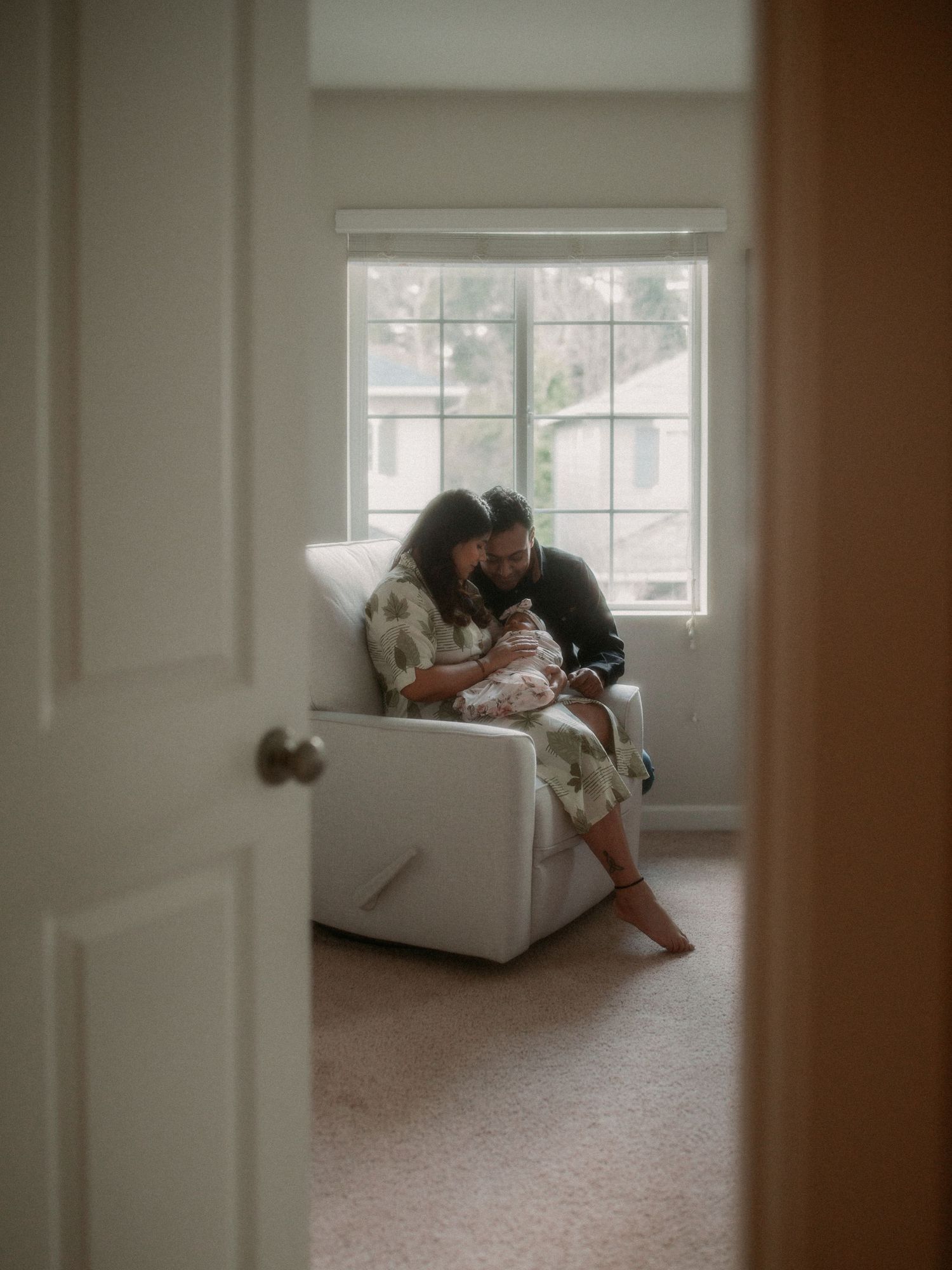 A quiet moment captured through a doorway showing two people in a white armchair by a window.