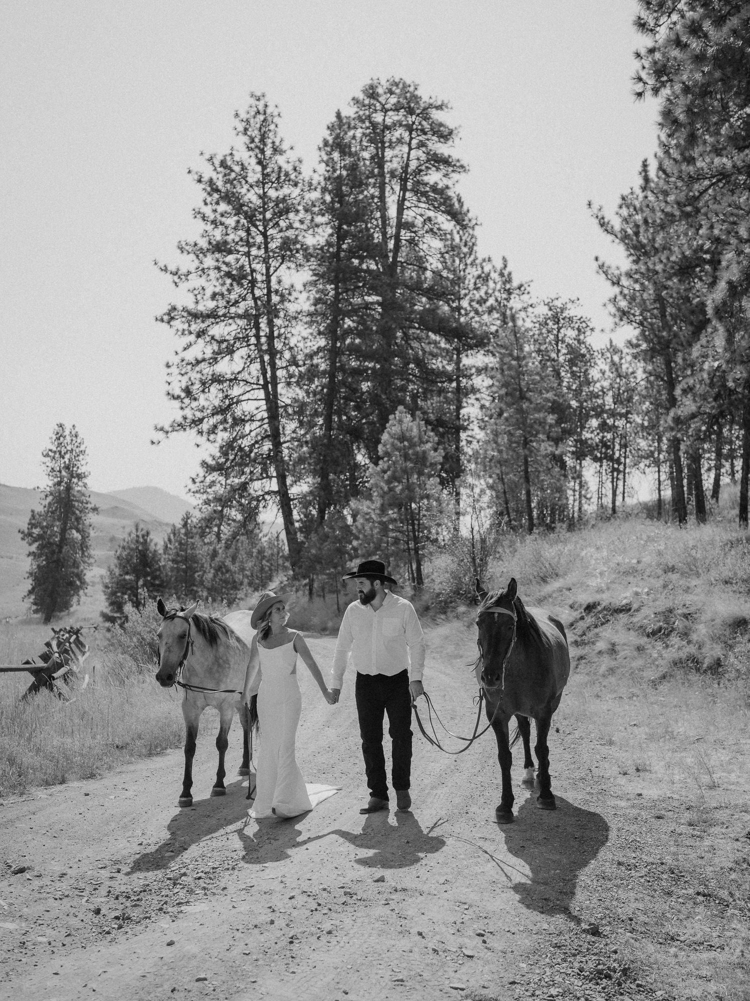 A black and white photo of a couple with horses on a mountain trail.