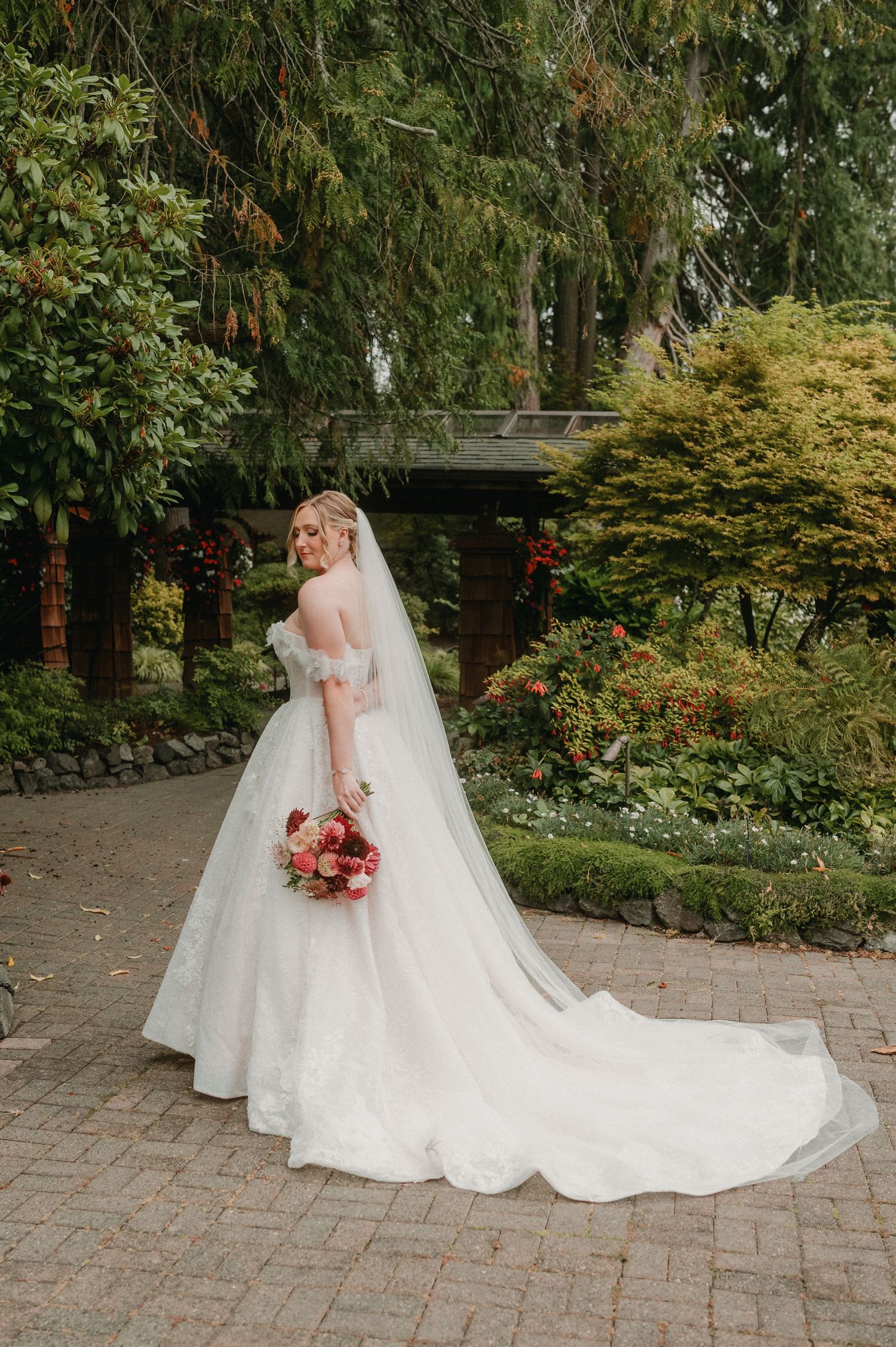 A beautiful bridal portrait series showing a flowing white wedding gown with long train on a brick patio surrounded by greenery.